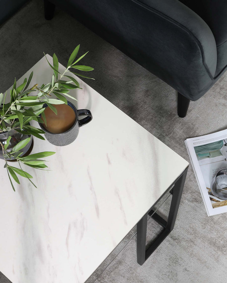 A contemporary marble-top coffee table with a minimalist black metal frame, positioned next to a dark upholstered sofa with visible sleek legs, all set on a textured grey area rug.