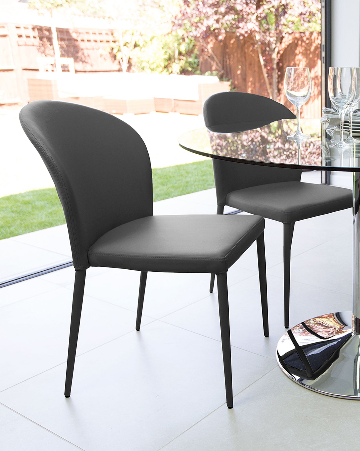 Elegant modern dining chairs in black, featuring a streamlined design with a curved backrest and a comfortable padded seat, set against a minimalist dining table with a reflective surface and cylindrical base.