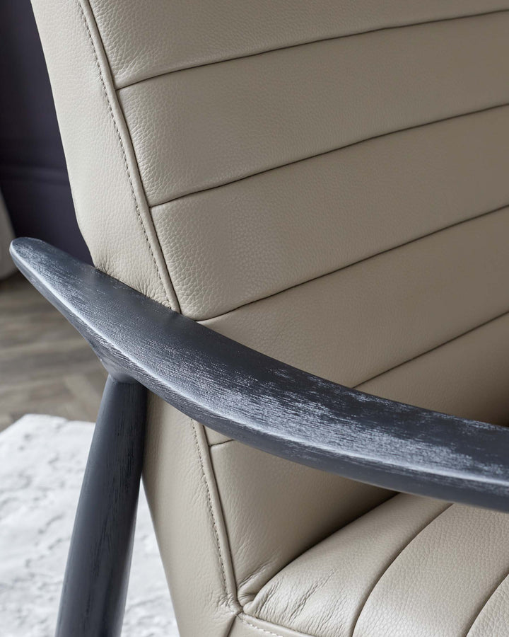 A close-up view of an upholstered chair featuring a cream-colored, textured leather back with horizontal stitching and a dark wooden armrest with a distressed finish.