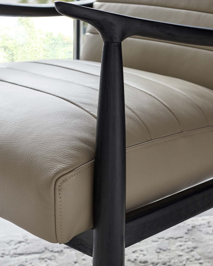 Close-up of a modern chair with beige leather upholstery and a dark wood frame, highlighting the quality and texture of the materials as well as the sleek design of the armrest.