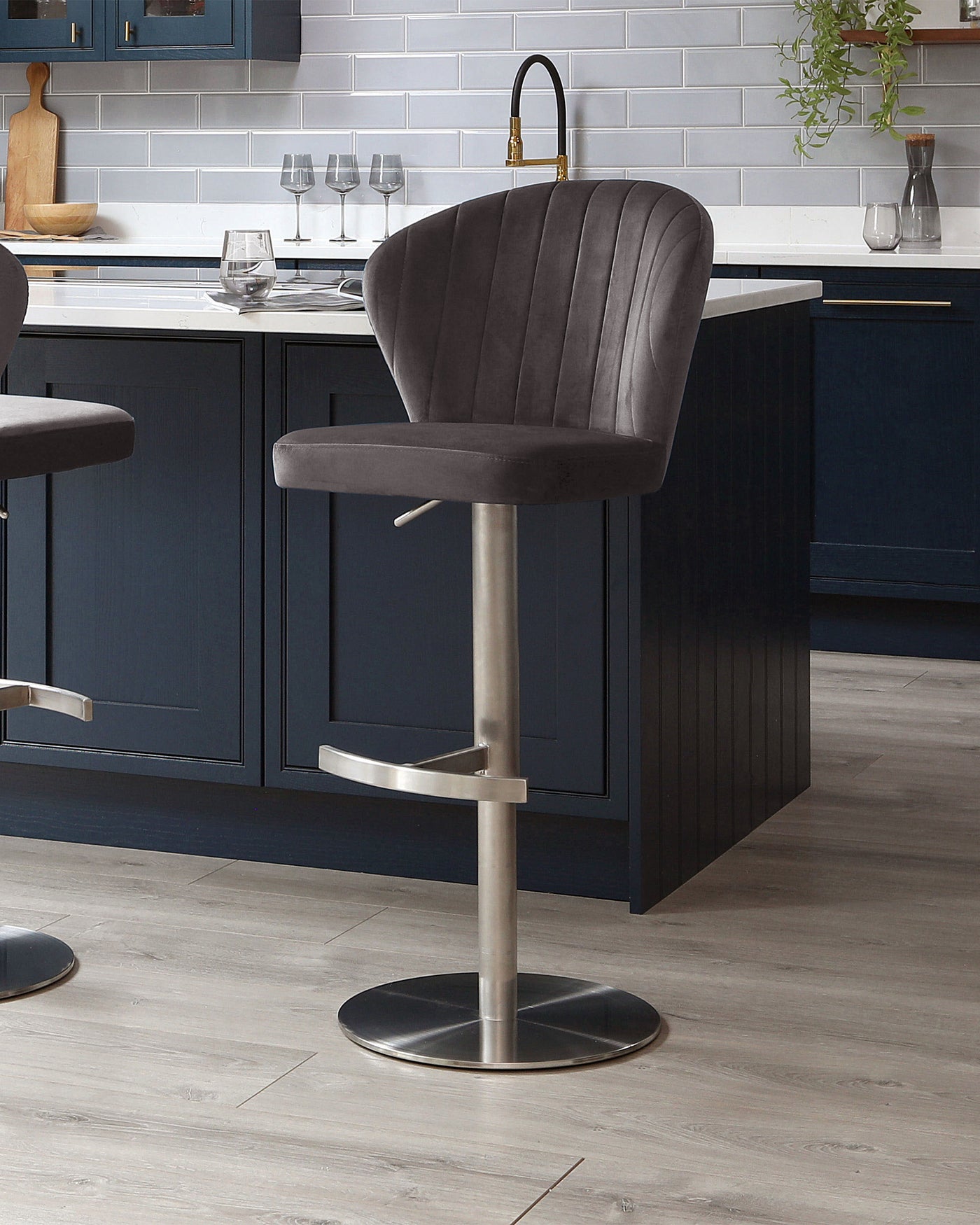 Elegant modern bar stool with a curved, channel-tufted backrest and plush seat upholstered in dark grey velvet fabric. The stool features an adjustable height mechanism, a sleek stainless steel pedestal base, and a built-in footrest for added comfort.