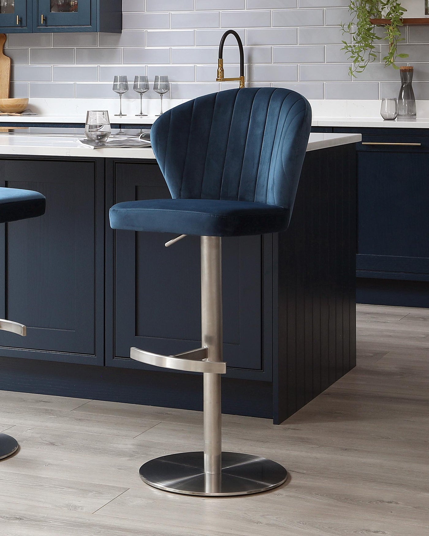 Elegant navy blue velvet bar stool featuring a curved backrest with vertical channel tufting and a sleek chrome pedestal base with a footrest and adjustable height mechanism.