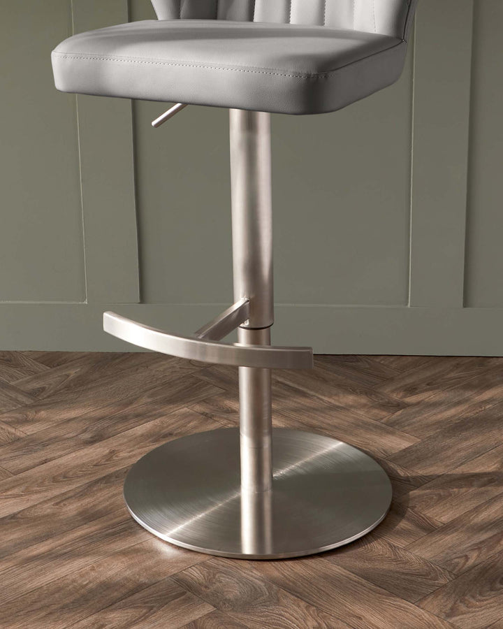 Modern adjustable bar stool with a brushed metal base, sleek footrest, and a padded grey faux leather seat with a low backrest.