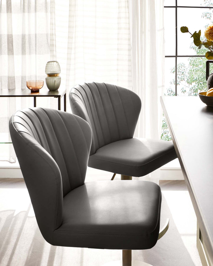 Two modern grey upholstered dining chairs with vertical channel tufting and a sleek, black metal base. A small round side table with a black frame and a wooden top, holding decorative vases, is visible in the background. The setting is illuminated by natural light from a large window with sheer curtains.