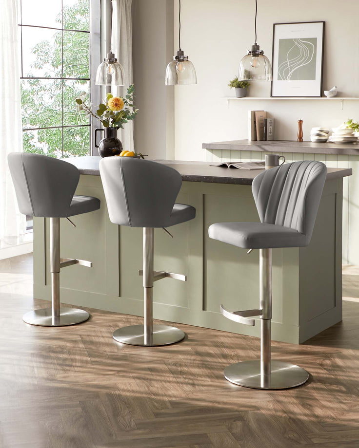 Three modern grey upholstered bar stools with tufted backrests and adjustable height features, supported by sleek metallic bases, are displayed in a bright kitchen setting with natural light.