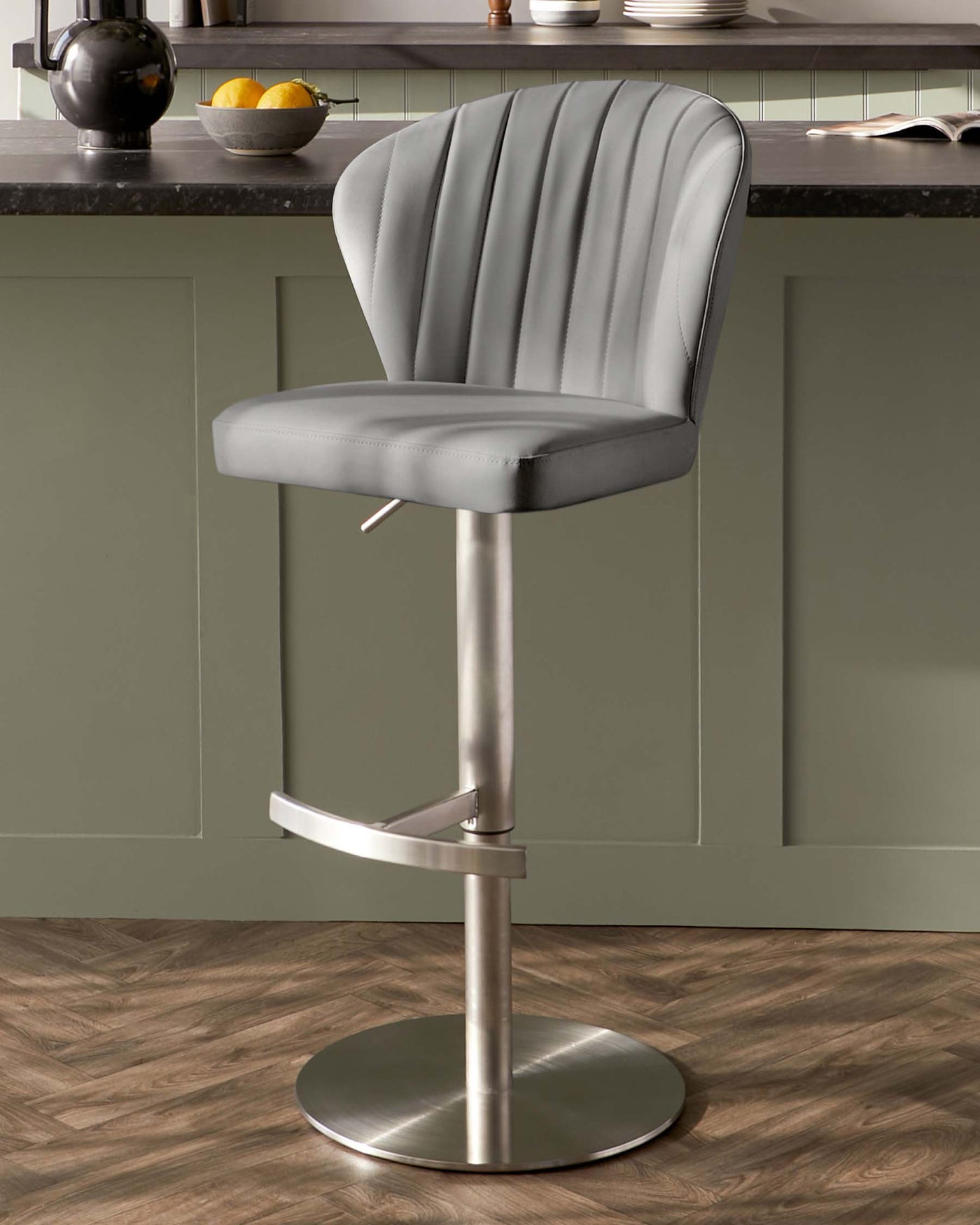 Modern grey upholstered bar stool with vertical channel tufting, a curved backrest, built-in footrest, and an adjustable height lever under the seat, set on a circular chrome base.