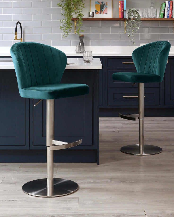 A pair of luxurious teal velvet bar stools with channel tufting on the backrests, featuring adjustable-height swivel seats, a footrest, and circular chrome bases.
