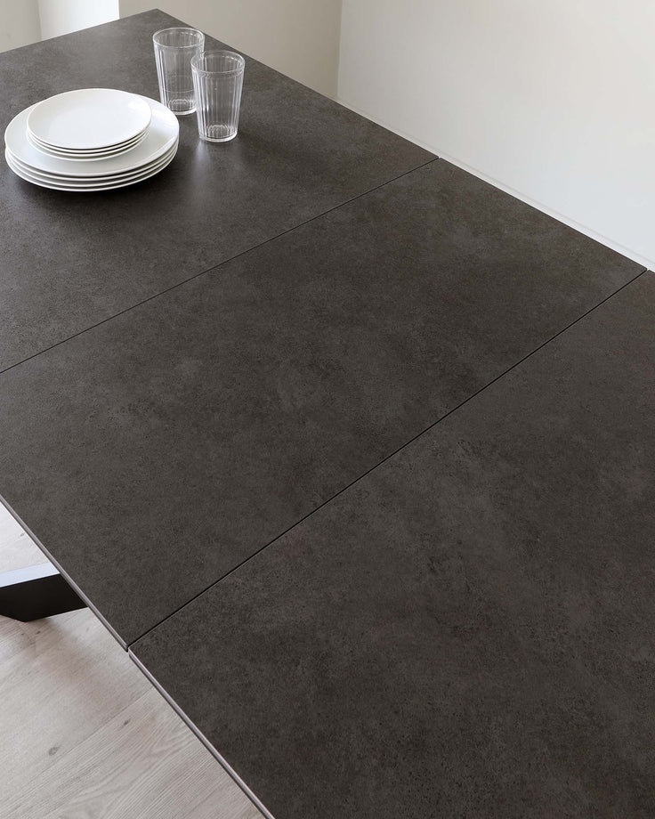 A dark grey stone-effect extendable dining table is set with plates and glasses.