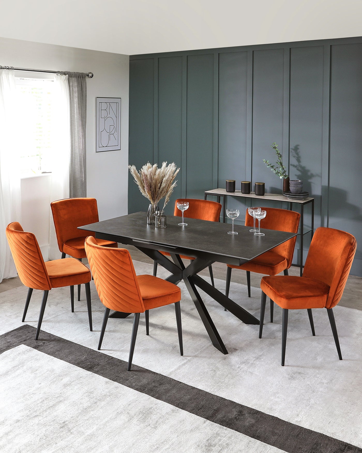 Modern dining room set featuring a black rectangular table with a unique angular leg design, accompanied by six burnt orange upholstered dining chairs with channel tufting and slim black metal legs, all placed on a grey and white striped area rug. A sideboard with decorative items is in the background.