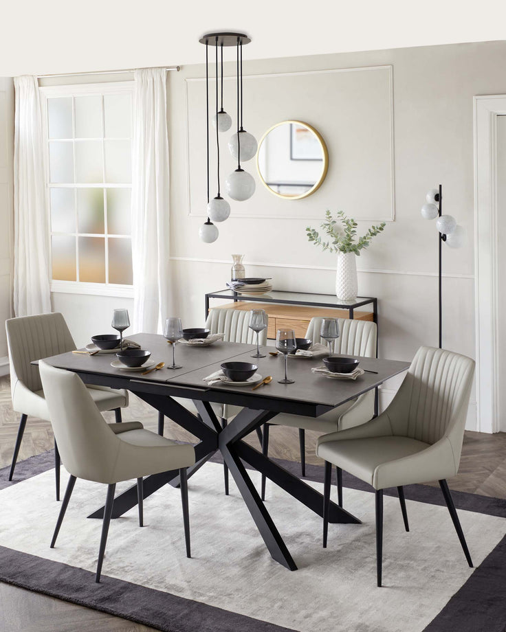 Modern dining room with a rectangular black table featuring a unique X-shaped leg design and six elegant light grey upholstered dining chairs with vertical stitching on the backrest. A minimalist black console table with simple straight lines and a smoked glass vase is also shown.