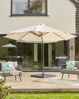 Outdoor seating with stylish cushions, a large umbrella for shade, and a patterned rug on a patio surrounded by greenery.