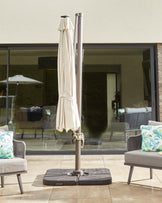An outdoor umbrella stand with a beige umbrella and two light gray lounge chairs, featuring colorful leaf-patterned cushions.