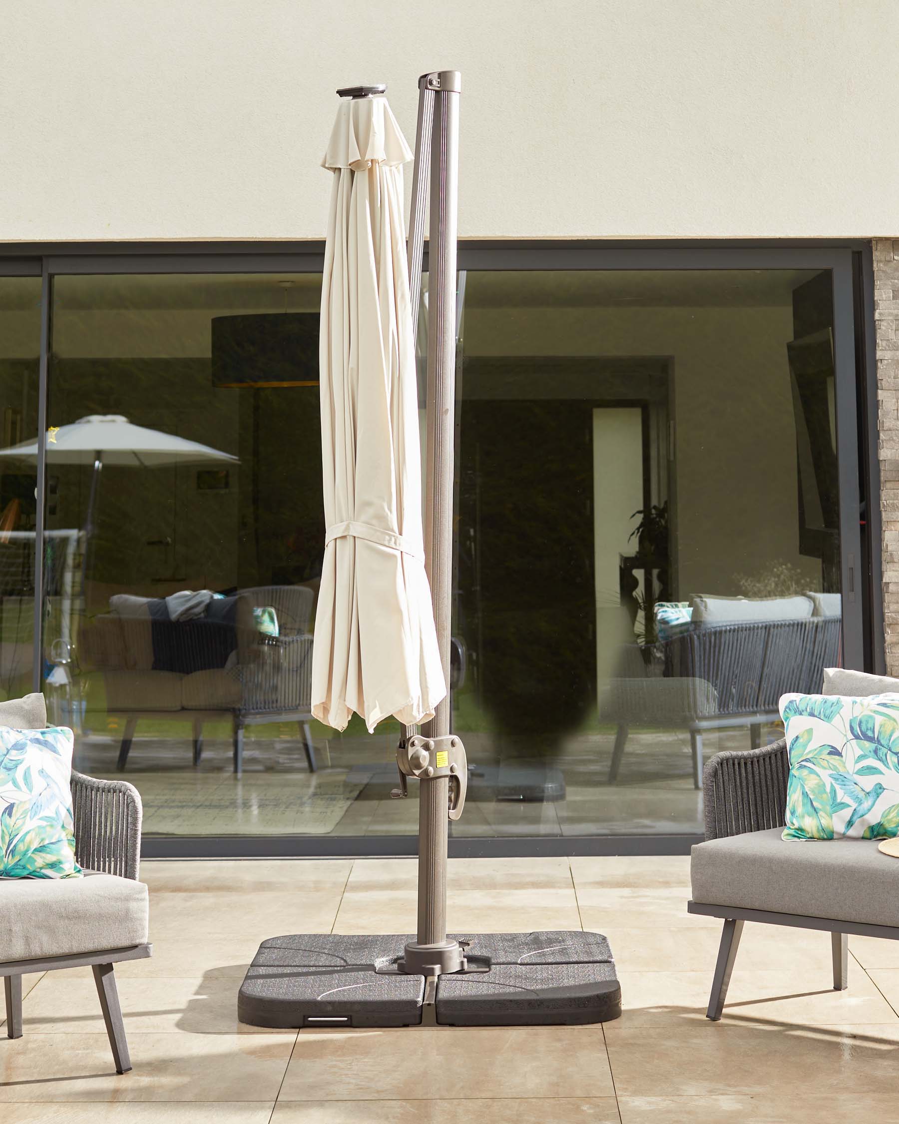 An outdoor umbrella stand with a beige umbrella and two light gray lounge chairs, featuring colorful leaf-patterned cushions.