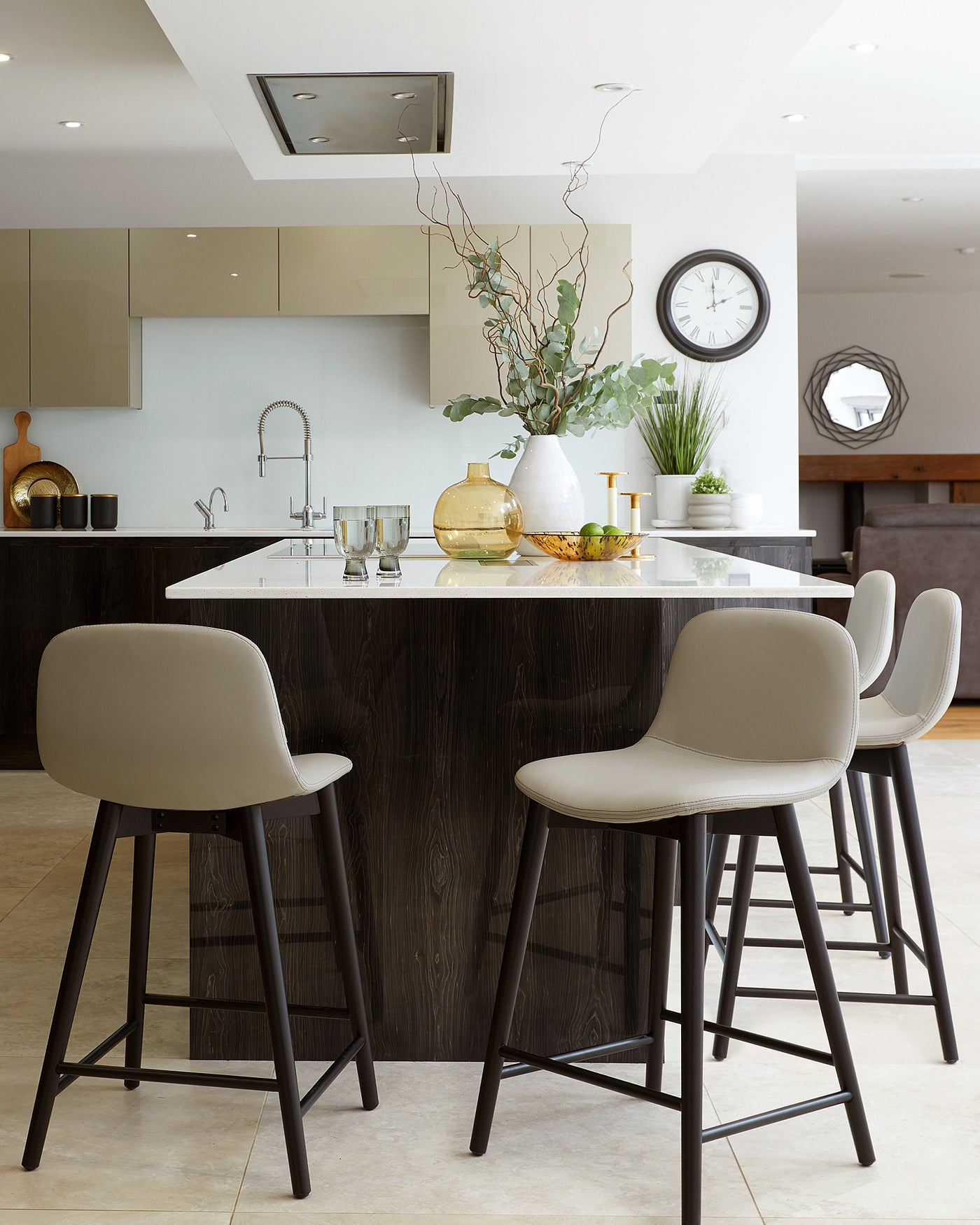 Modern kitchen with three stylish bar stools featuring dark wooden legs and comfortable, curved light grey seats, arranged at a kitchen island with a dark wood finish and white countertop.