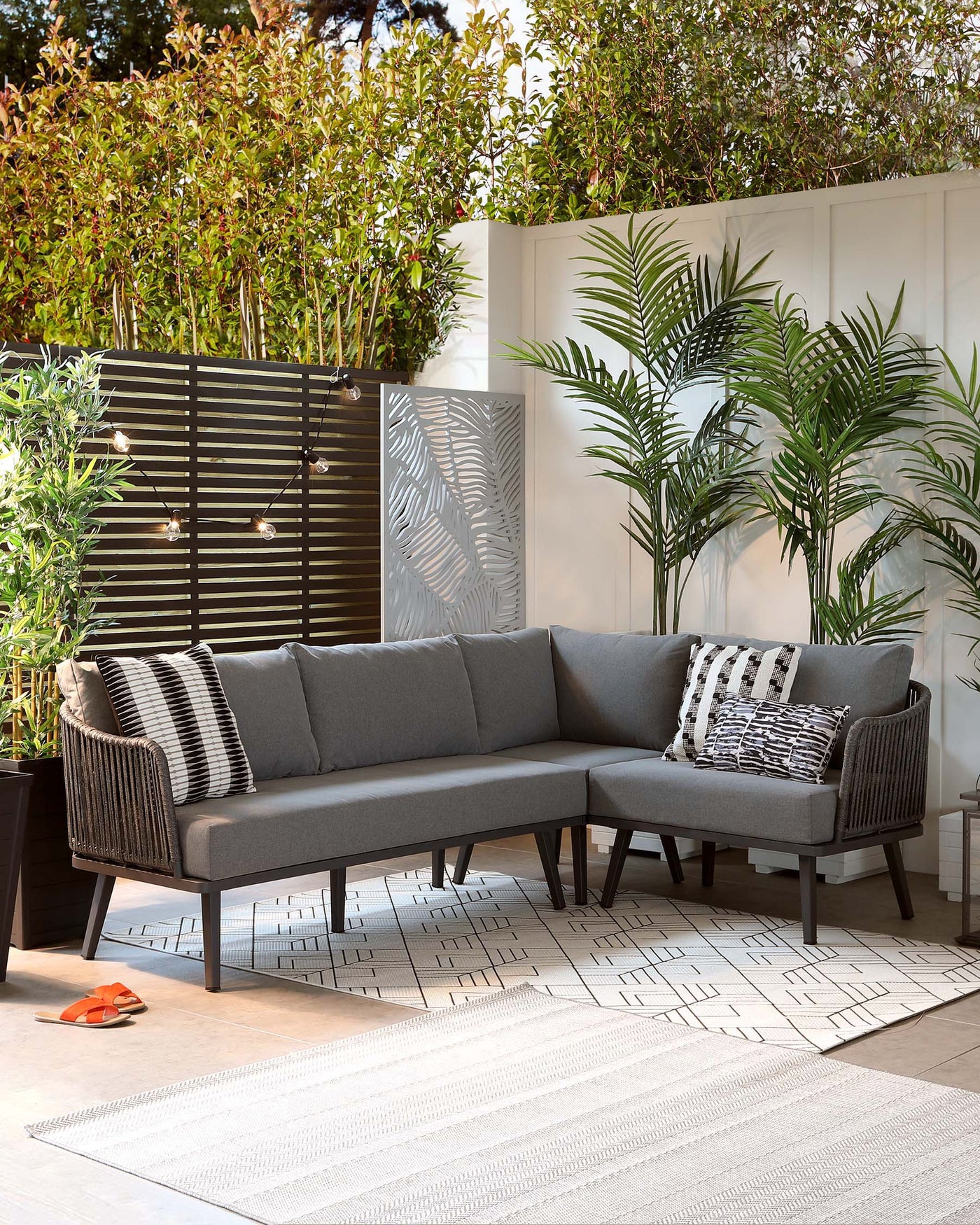L-shaped outdoor sectional sofa with grey upholstered cushions and woven side detailing on a geometric-patterned area rug.