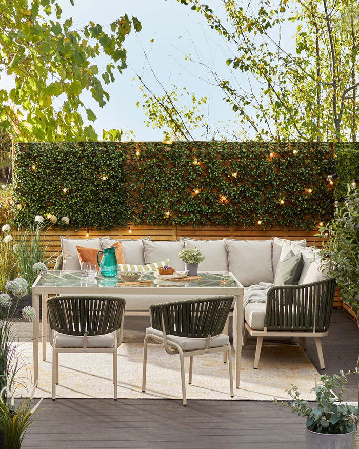 Outdoor patio furniture set including a sectional sofa with light grey cushions, a modern rectangular glass-topped dining table, and four contemporary-style dining chairs with grey straps and cushions, set on a wooden deck with ambient string lights and greenery in the background.
