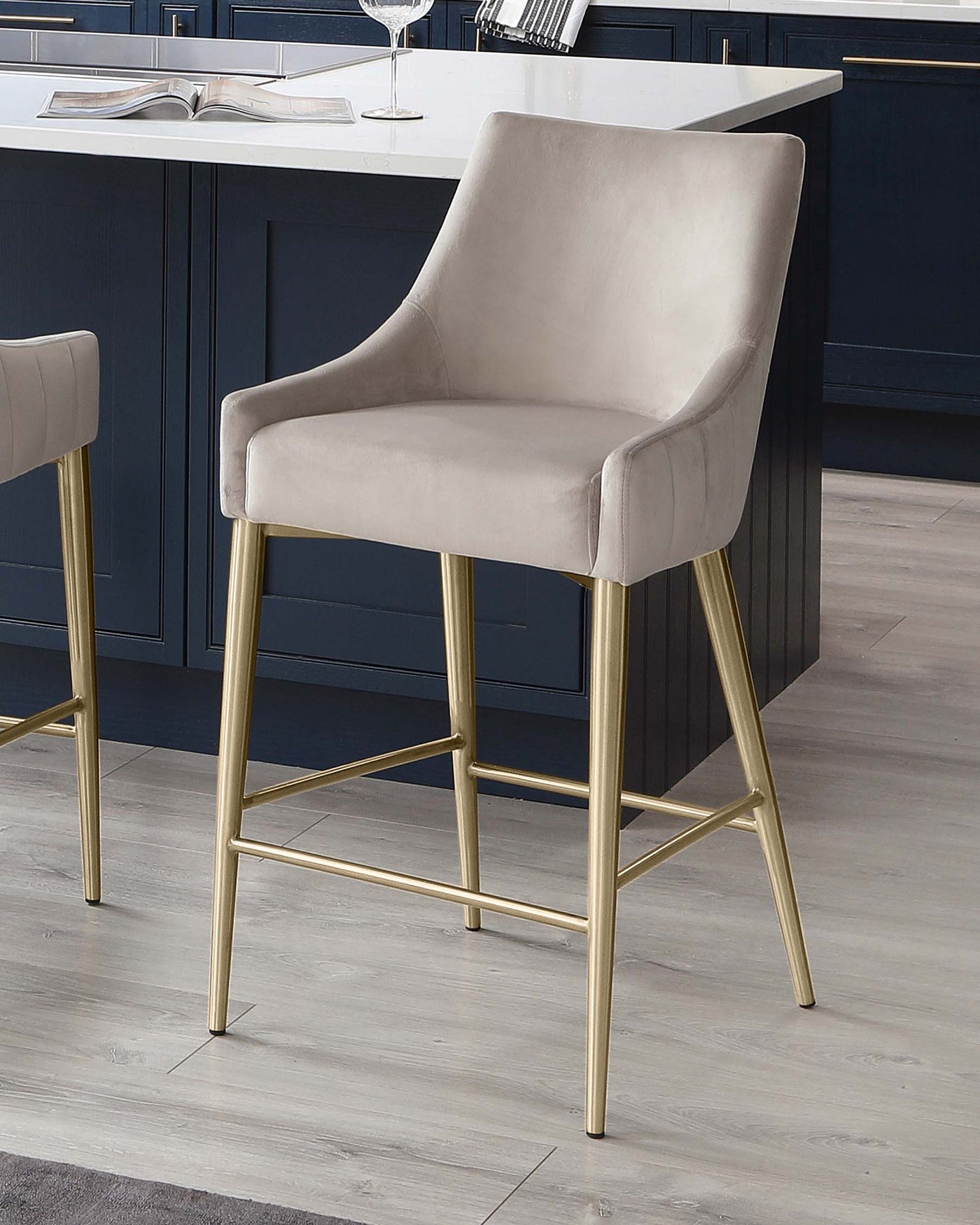 Elegant modern bar stool with a beige velvet upholstered seat and backrest, featuring sleek armrests, and supported by a sturdy gold-finished metal frame with footrests.
