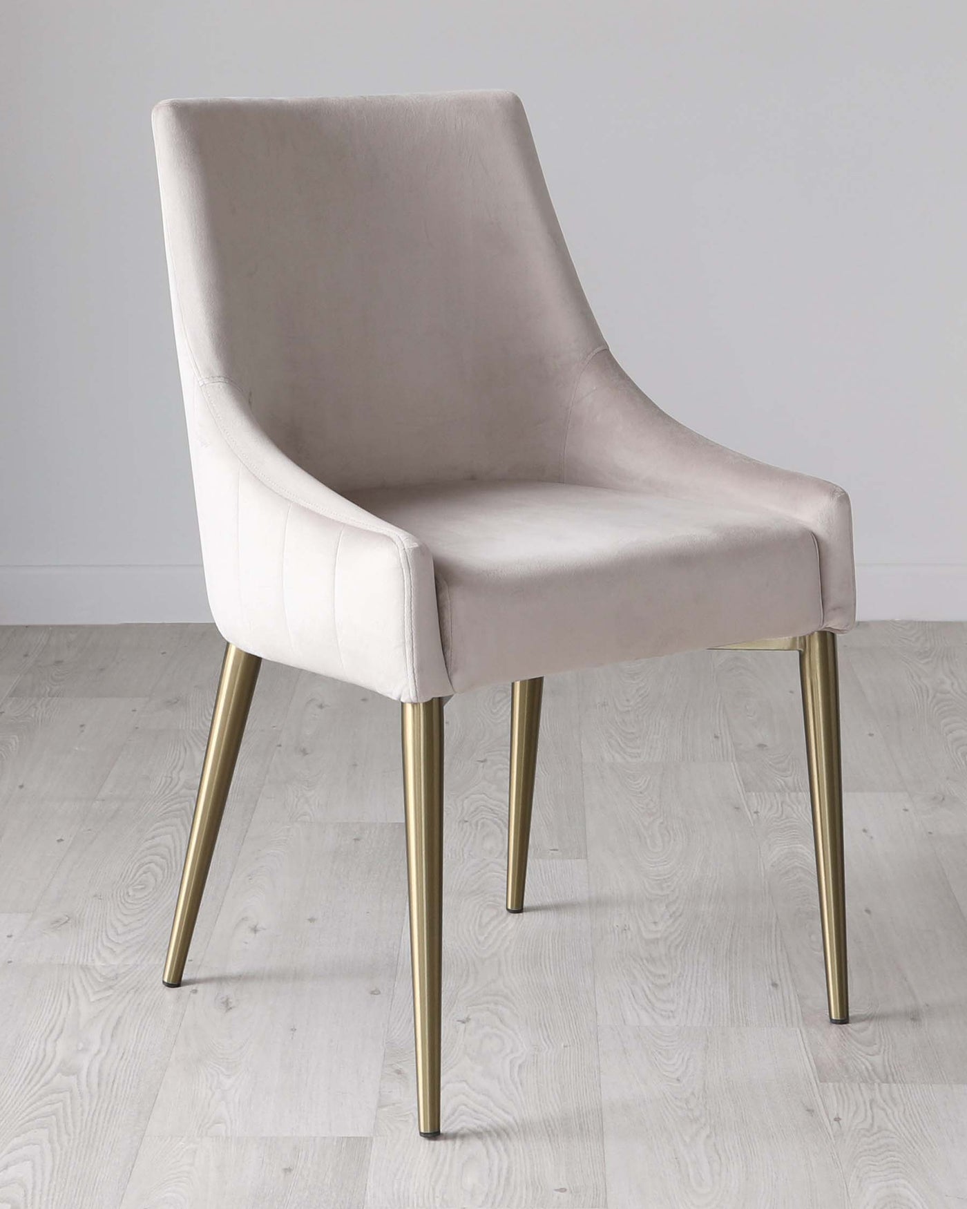 Elegant modern dining chair with a soft velvety beige upholstery and vertical stitching on the backrest, featuring sleek tapered metal legs in a brushed gold finish.