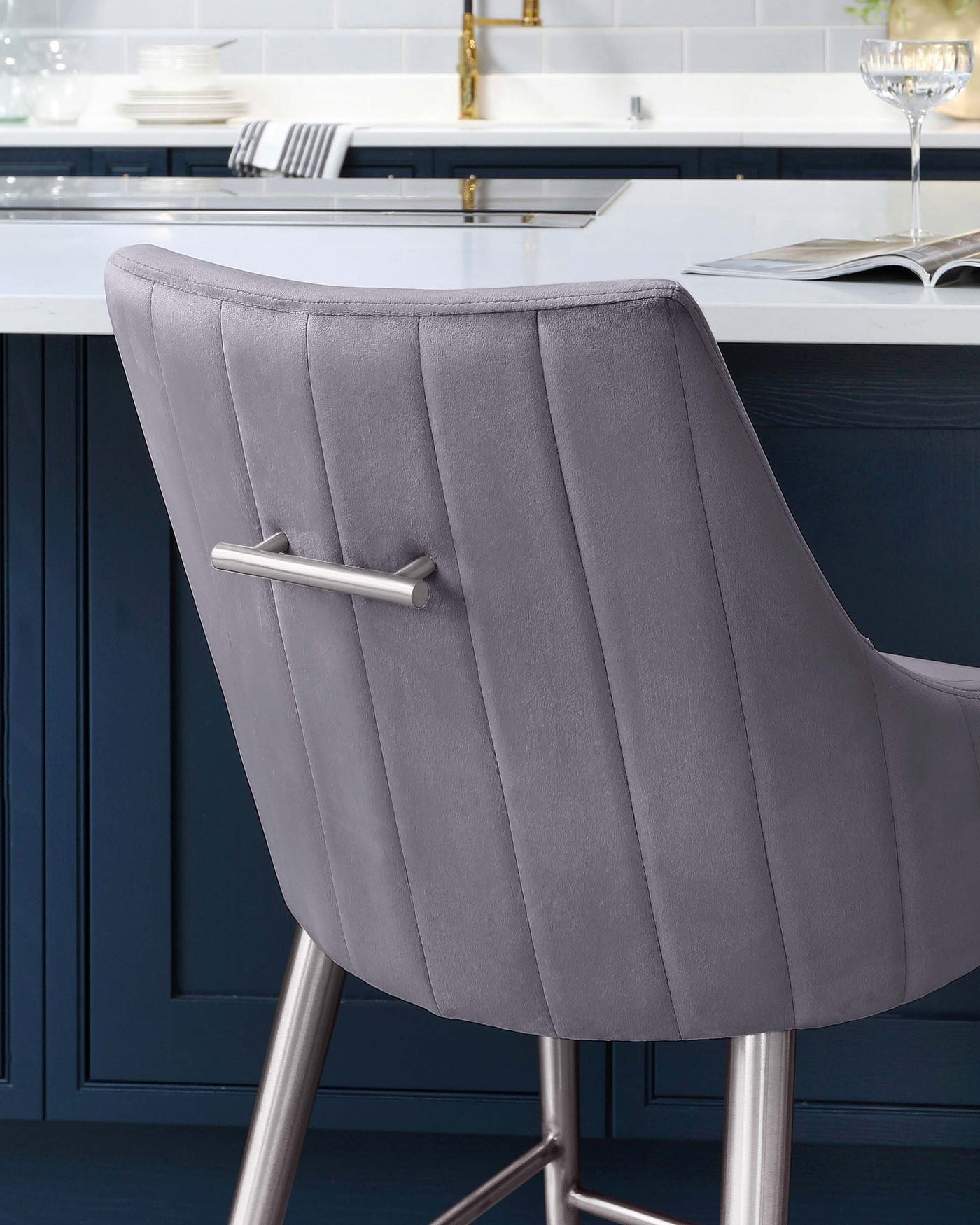 Elegant modern bar stool with a high backrest, upholstered in a soft grey fabric with vertical stitching, featuring a sleek chrome pedestal base with a footrest.