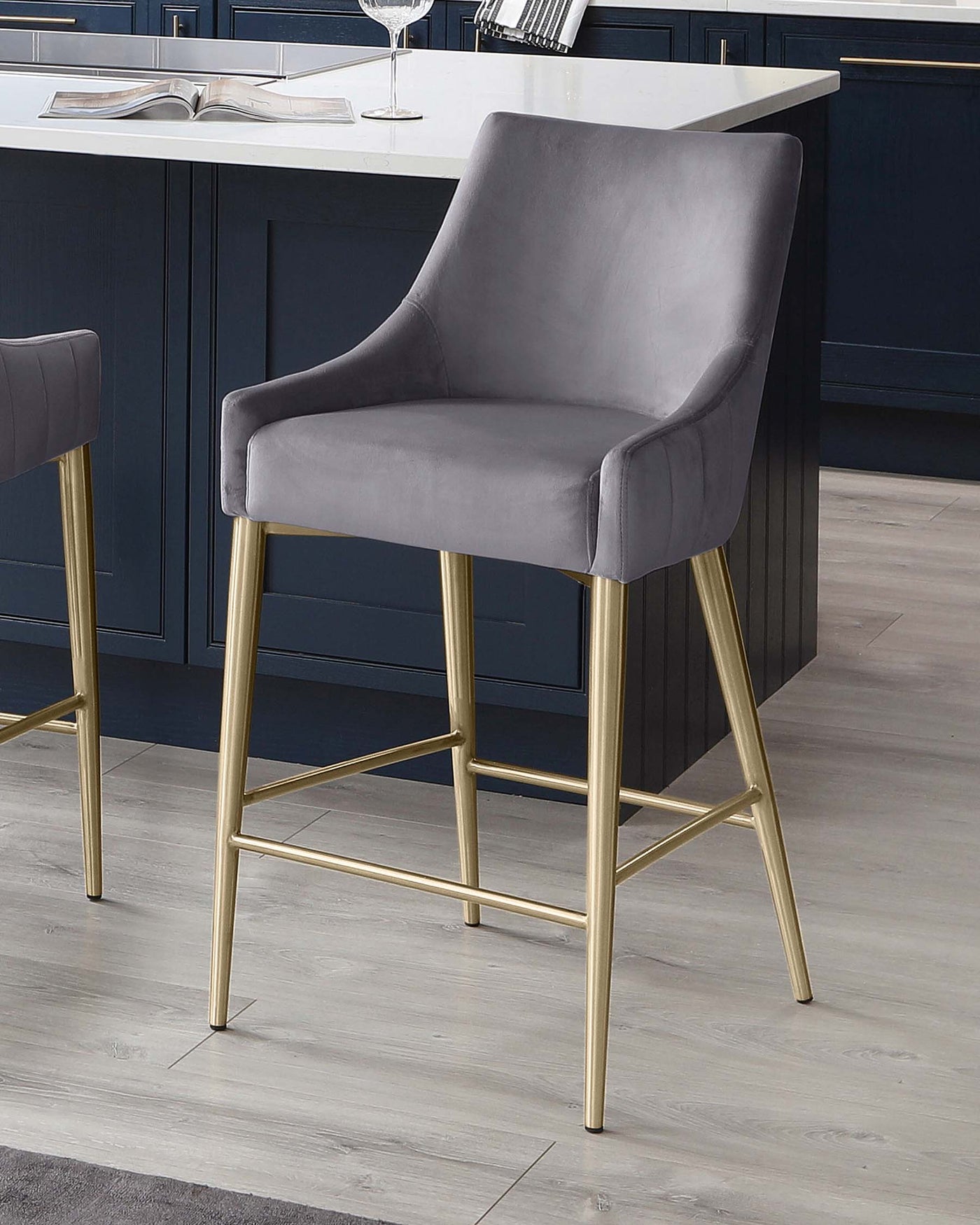 Elegant grey velvet barstool with a curved backrest and armrests, featuring sleek gold metal legs with a square footrest.