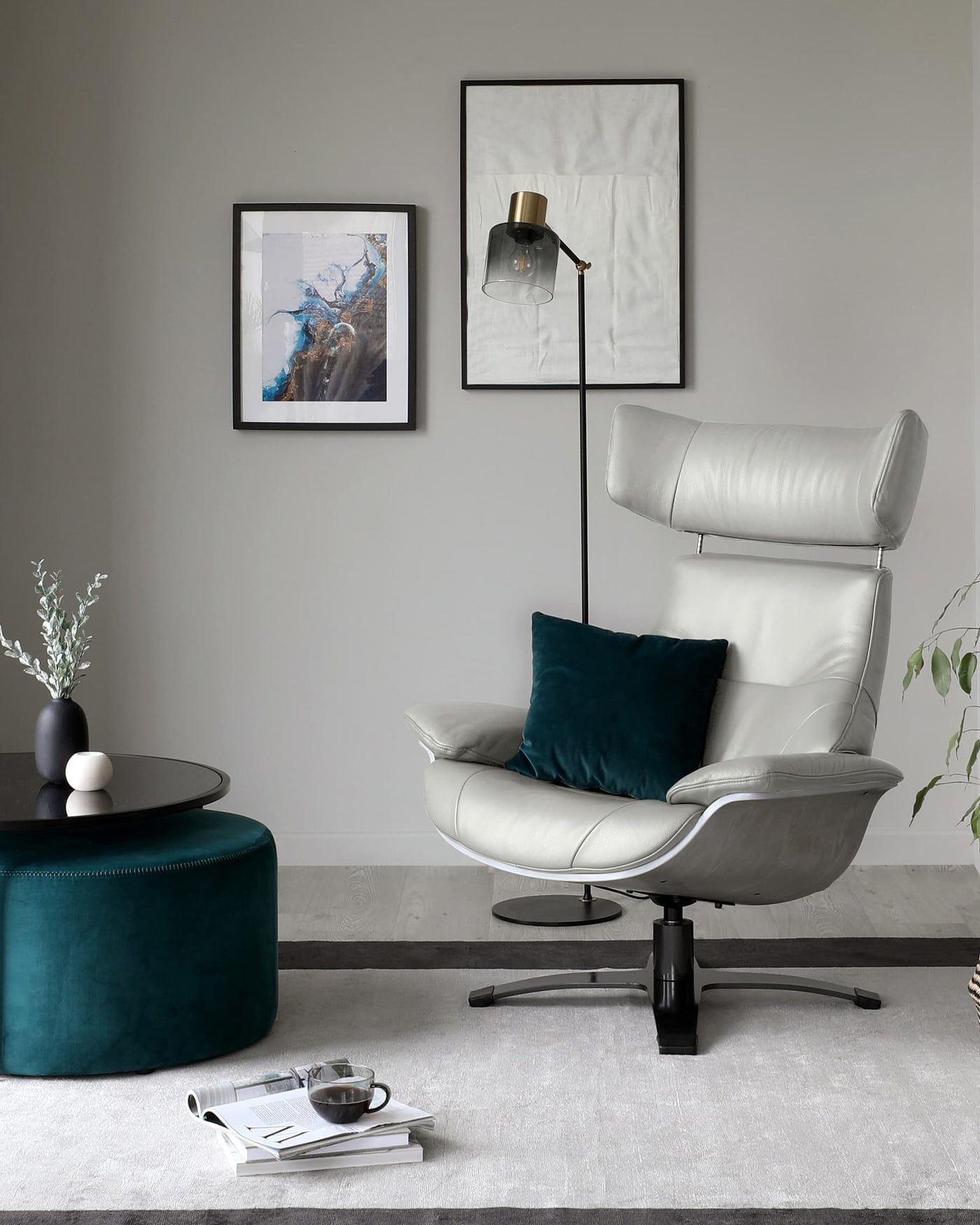 Modern living room setup with a sleek white leather recliner featuring a curved backrest and a contoured seat, complemented by a plush teal accent pillow. A round black coffee table with a matte top and a cylindrical emerald green velvet ottoman add a touch of luxe and colour contrast to the space. A white area rug anchors the arrangement, enhancing the minimalist and chic ambiance.