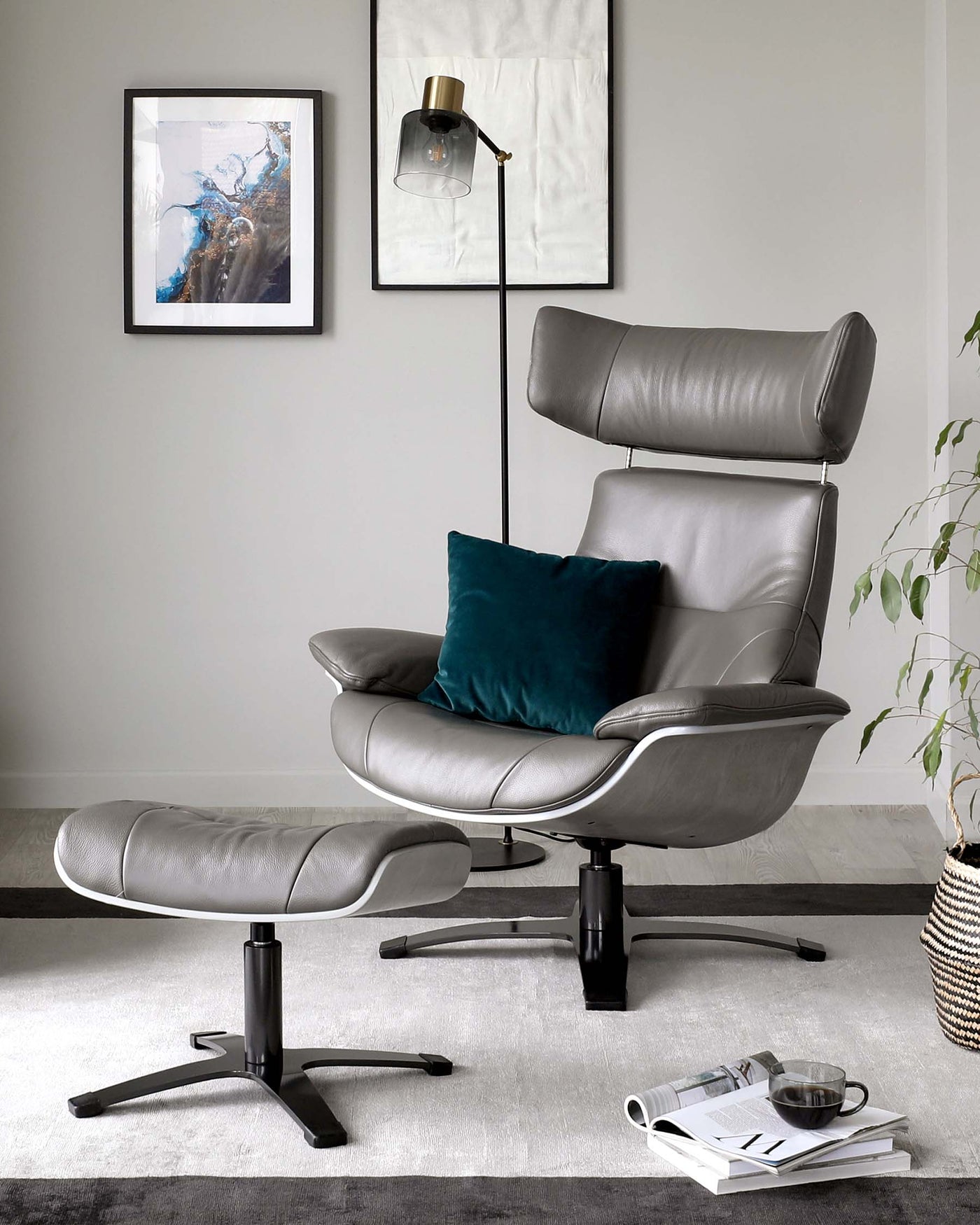 A modern grey leather recliner chair with an adjustable headrest and a matching leather ottoman set upon a black base. Both pieces feature sleek, curved lines and a swivel function. A velvety teal throw pillow adds a pop of colour to the chair. The set is positioned on a two-tone grey area rug in a contemporary-styled room.