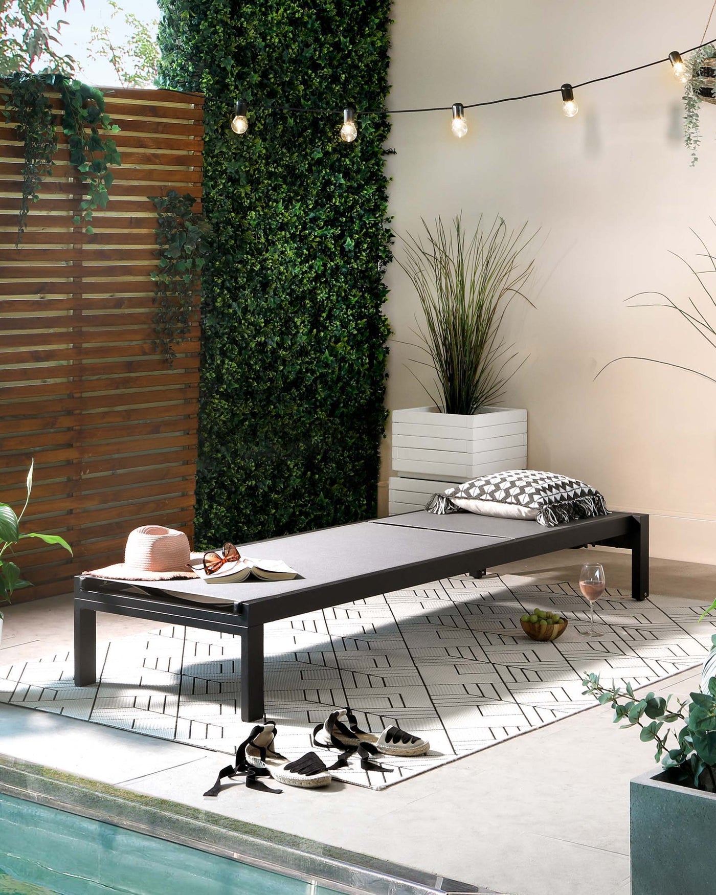 Sophisticated outdoor setting featuring a sleek, modern lounging daybed with a matte black frame and grey cushioning. A stylish black and white patterned outdoor rug anchors the space, complementing the contemporary look.
