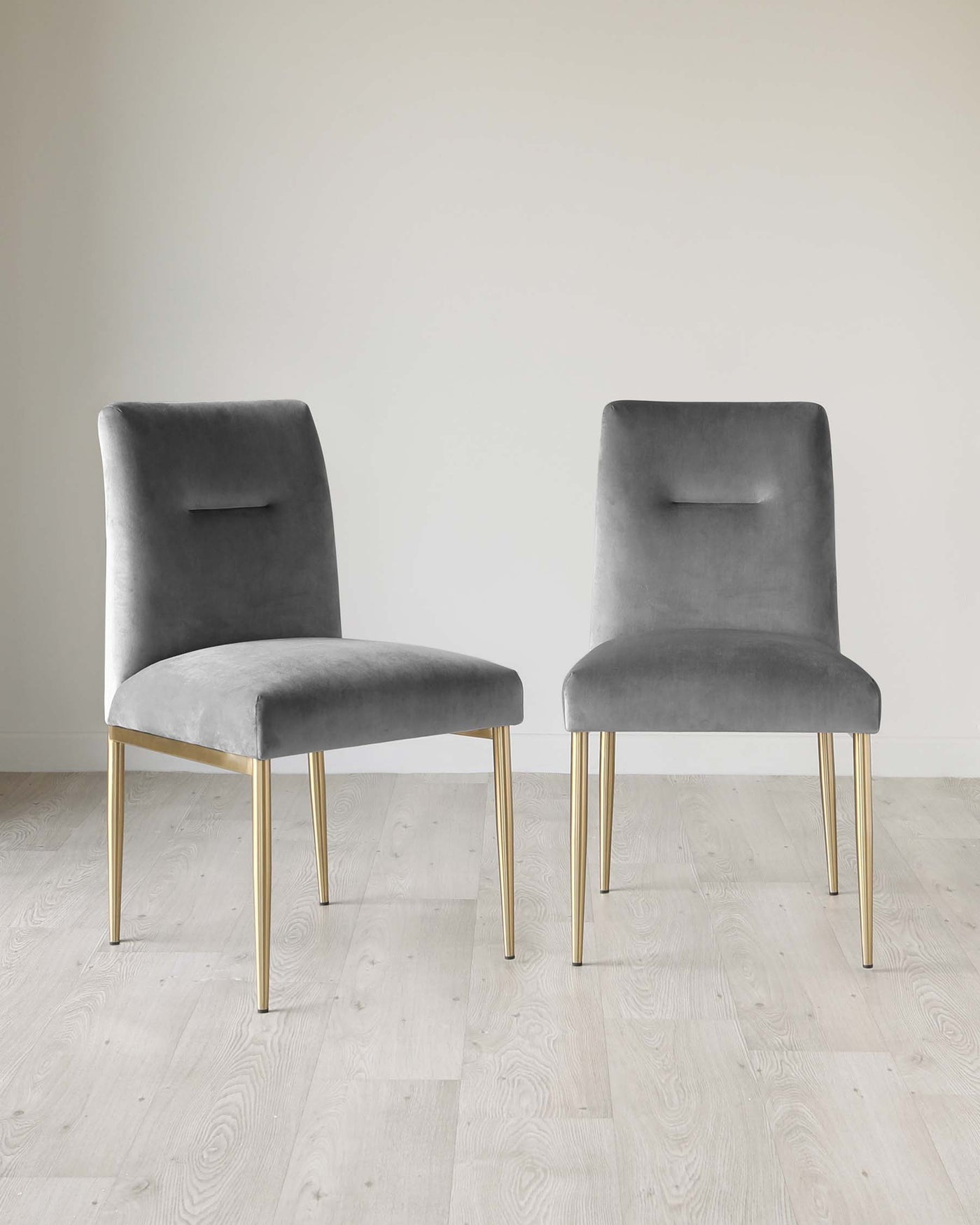 Two modern grey velvet dining chairs with sleek gold metal legs, featuring a simple and elegant design with a small cut-out detail on the backrest.