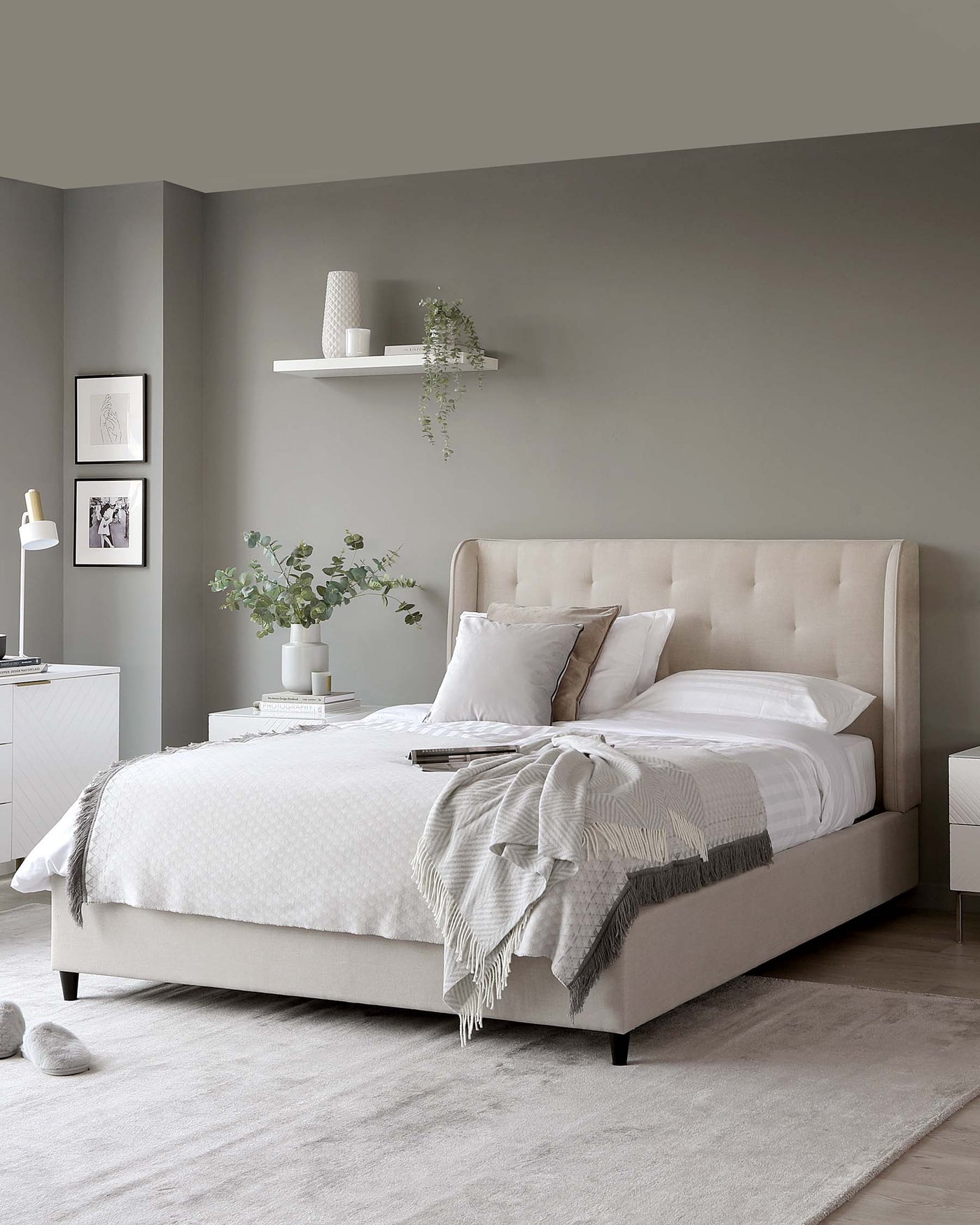 Elegant contemporary bedroom furniture featuring a beige upholstered bed with a high headboard and a white bedside table with minimalist design. Both pieces complement the neutral-toned decor.