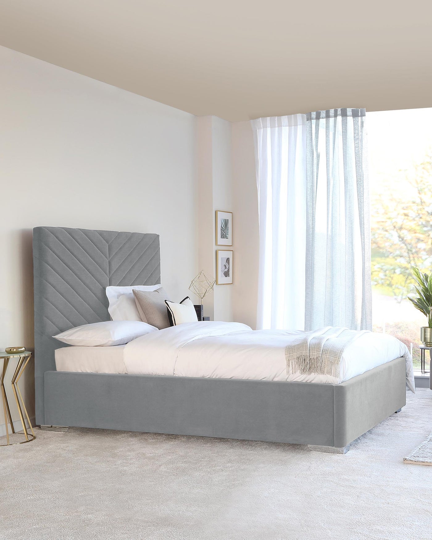 Elegant grey upholstered king-size platform bed with a high headboard featuring vertical channel tufting. Beside the bed is a gold metal side table with a cylindrical base and a round top.