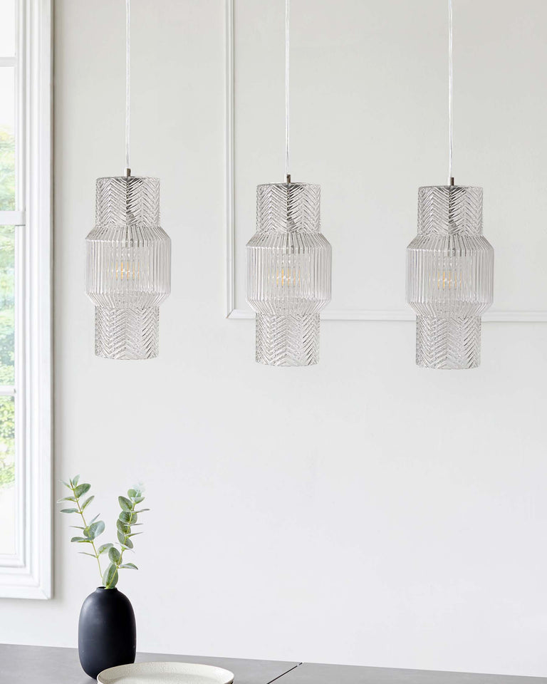 Three textured glass pendant lights hanging in a staggered formation with a modern geometric design, positioned above a subtle minimalist setting with a sleek vase and greenery.