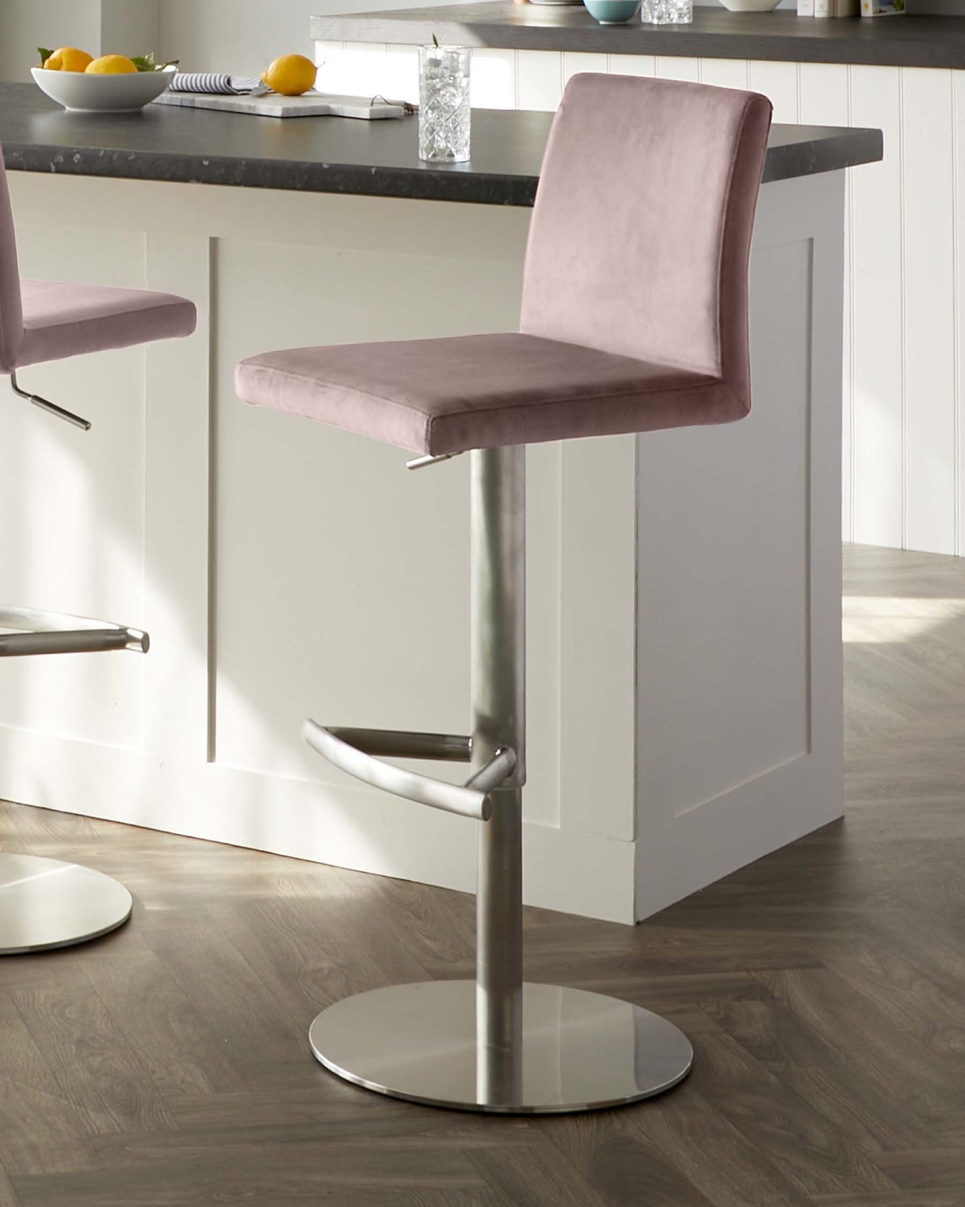 Modern adjustable-height bar stool with a smooth velvet seat in a muted pink tone, featuring a low backrest and an integrated footrest on a sleek metal pedestal base with a round, flat base plate.