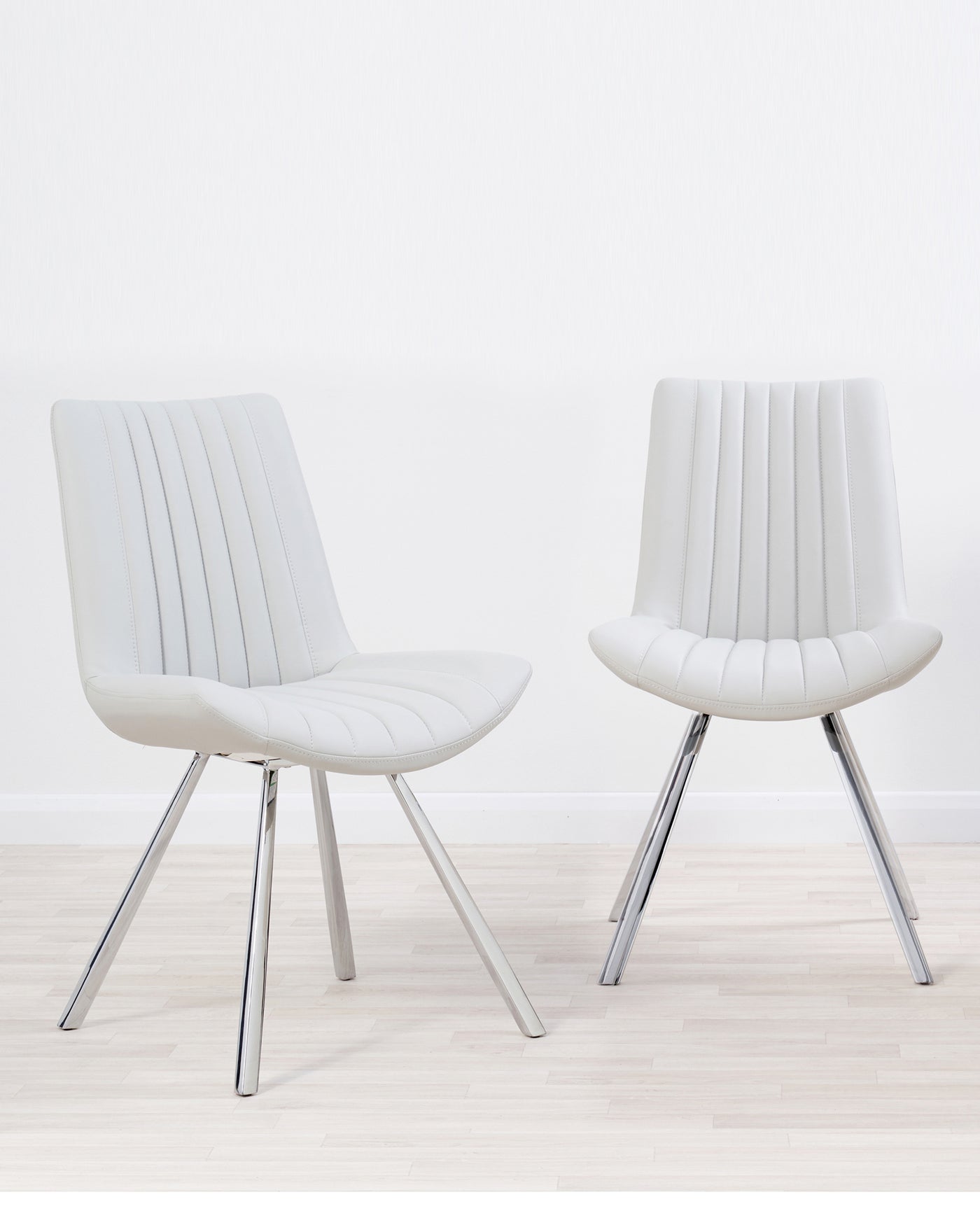 Two modern white leather dining chairs with vertical stitching and sleek chrome legs on a light wooden floor with a white background.