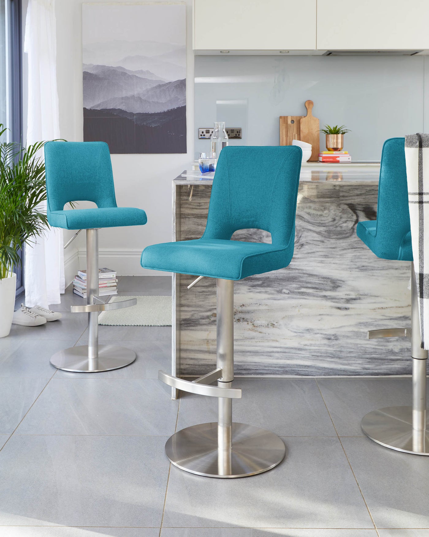 Teal blue contemporary bar stools with backrests, cushioned seats, and footrests on sleek, adjustable stainless steel pedestals.