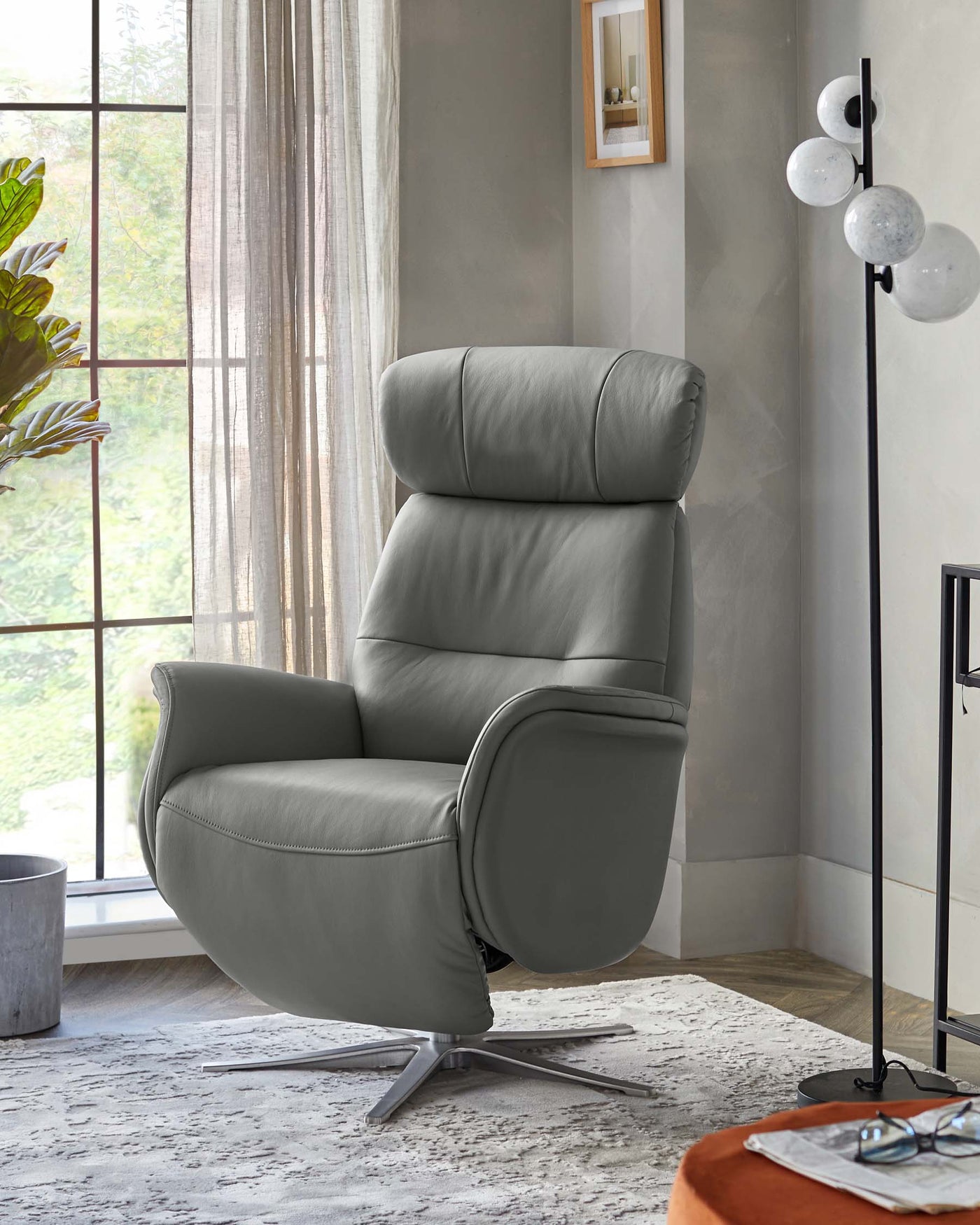 Modern grey leather recliner chair with a sleek design featuring a tufted backrest, padded arms, and a brushed metal swivel base, set in a stylish living room with natural light.