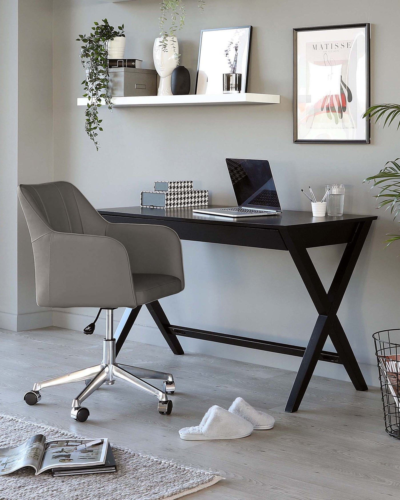 Contemporary home office setup featuring a sleek black desk with X-shaped legs and a light grey upholstered office chair with a high back and armrests, mounted on a shiny chrome base with casters for mobility.