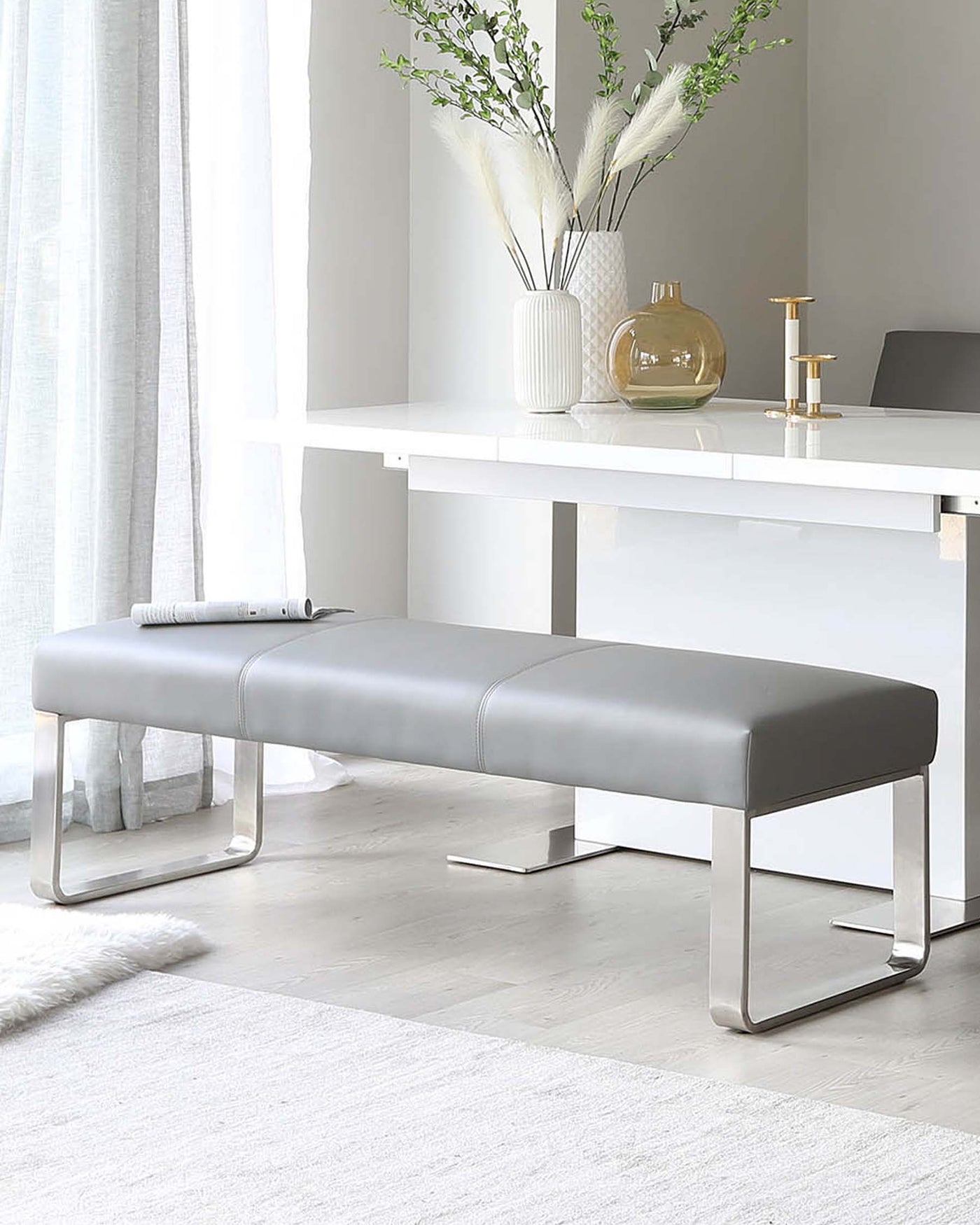 Modern minimalist furniture set including a sleek white desk with a clean, rectangular design and a grey upholstered bench with a chrome base, offering a contemporary look for a stylish home office or living space.