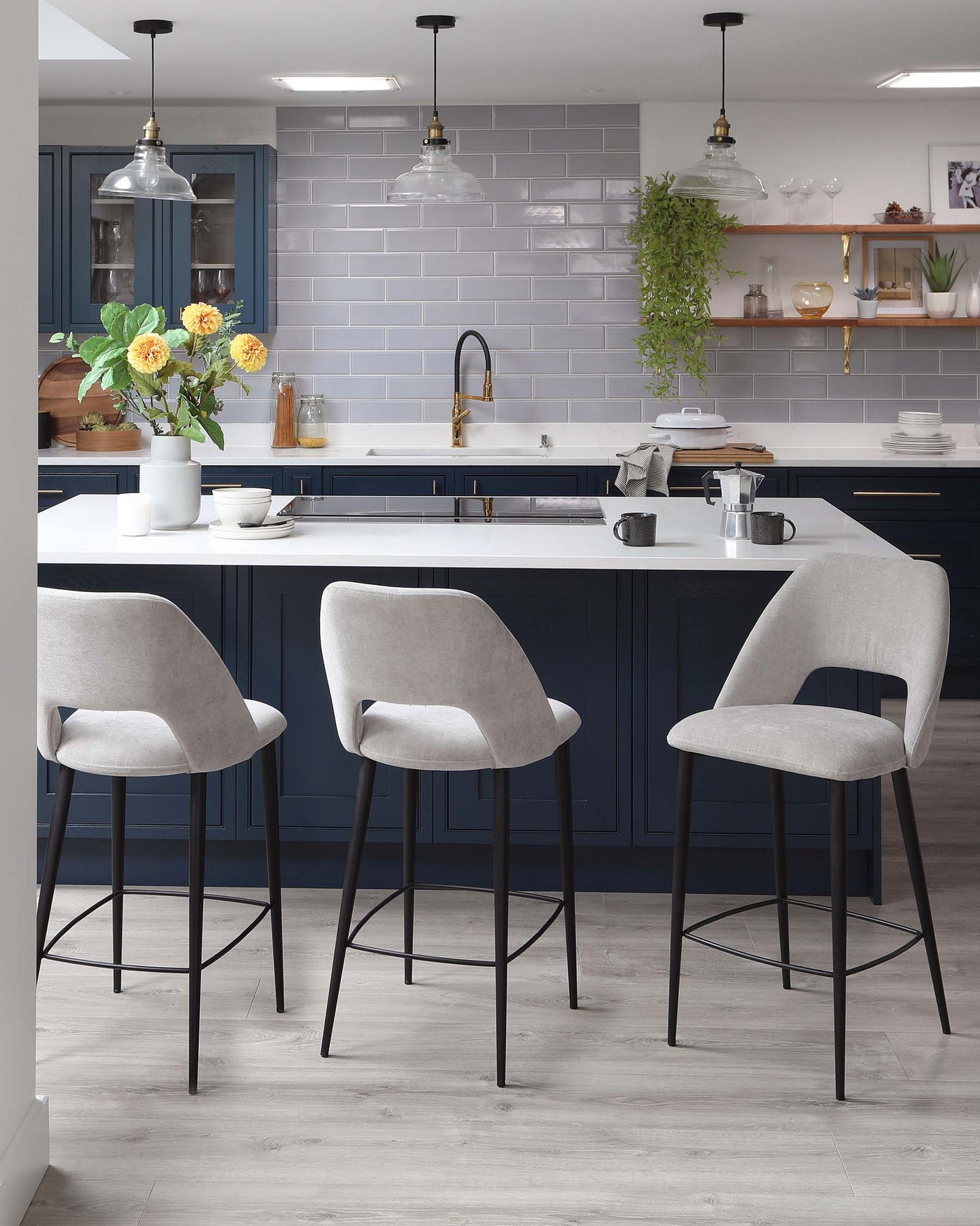 Three modern upholstered bar stools with sleek legs and footrests at a kitchen island.