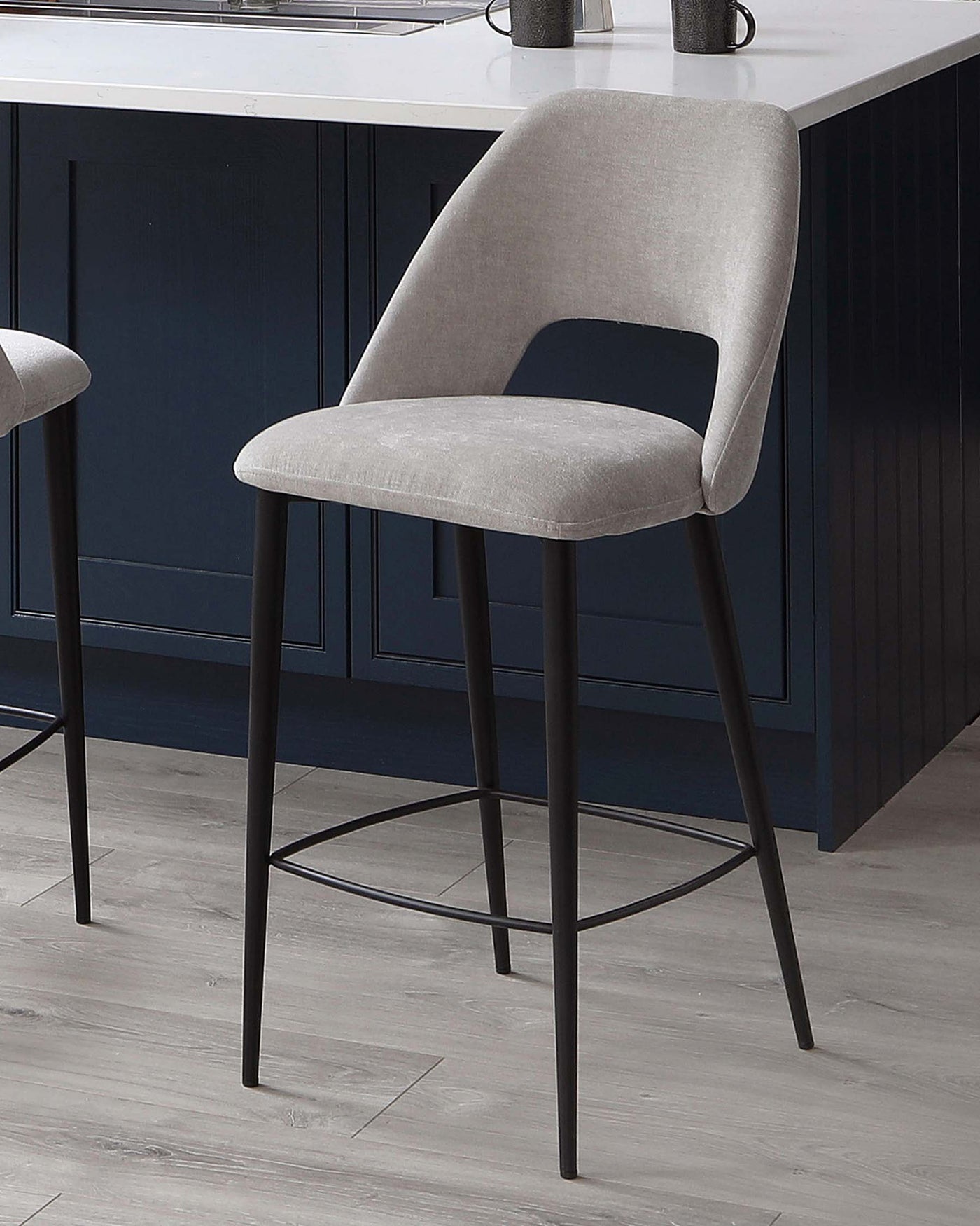 Modern light grey upholstered bar stool with a curved backrest and a cutout detail, mounted on a sleek black metal frame with four legs and footrest. Ideal for contemporary kitchen or bar settings.