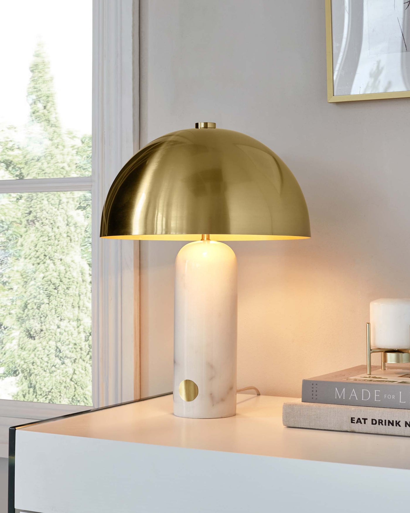 Elegant marble table lamp with a brass dome shade on a white modern tabletop, next to decor books.
