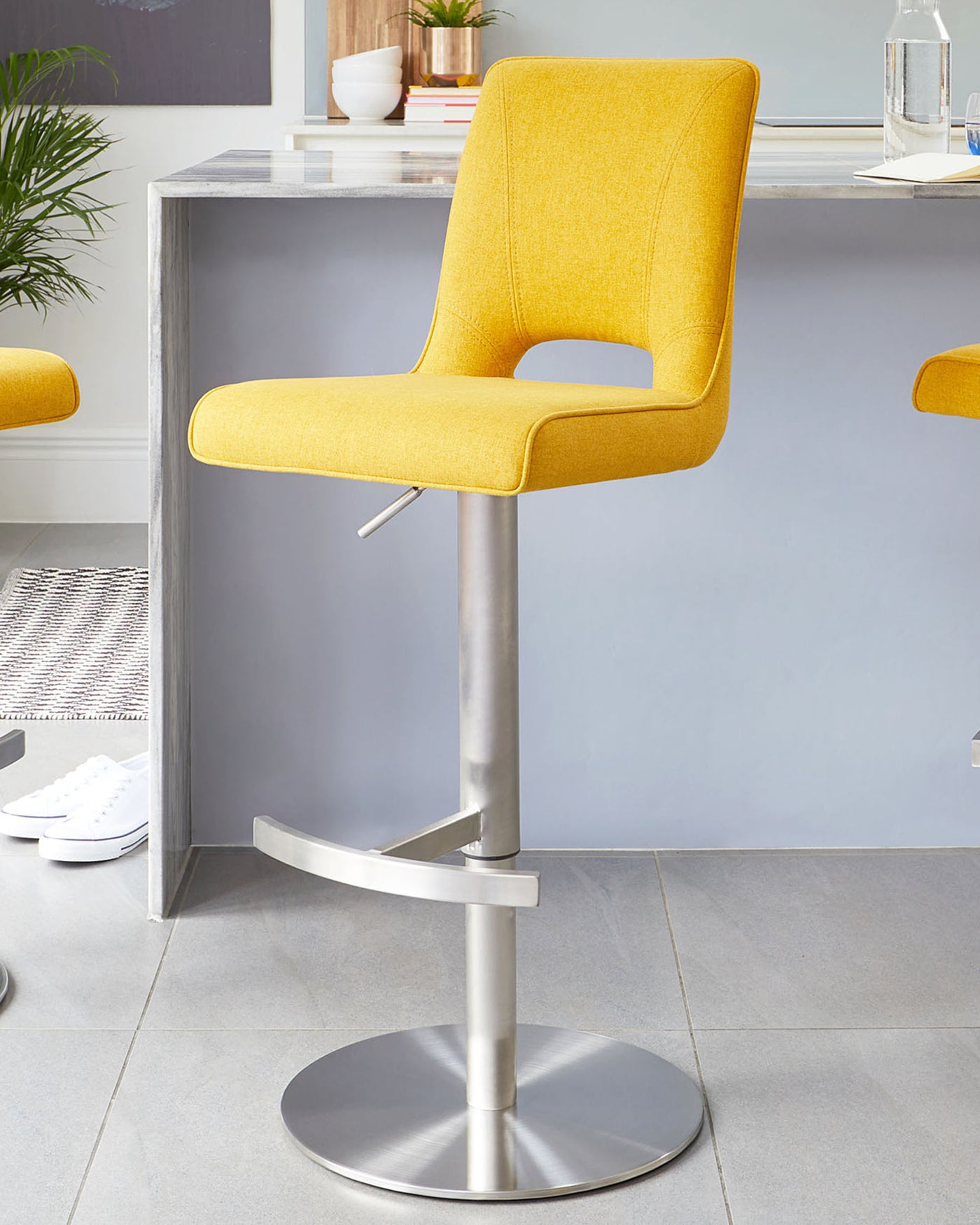 Modern adjustable-height barstool with a vibrant yellow upholstered seat, featuring clean lines, an ergonomic curved backrest with a cut-out detail, and a sleek metallic pedestal base.