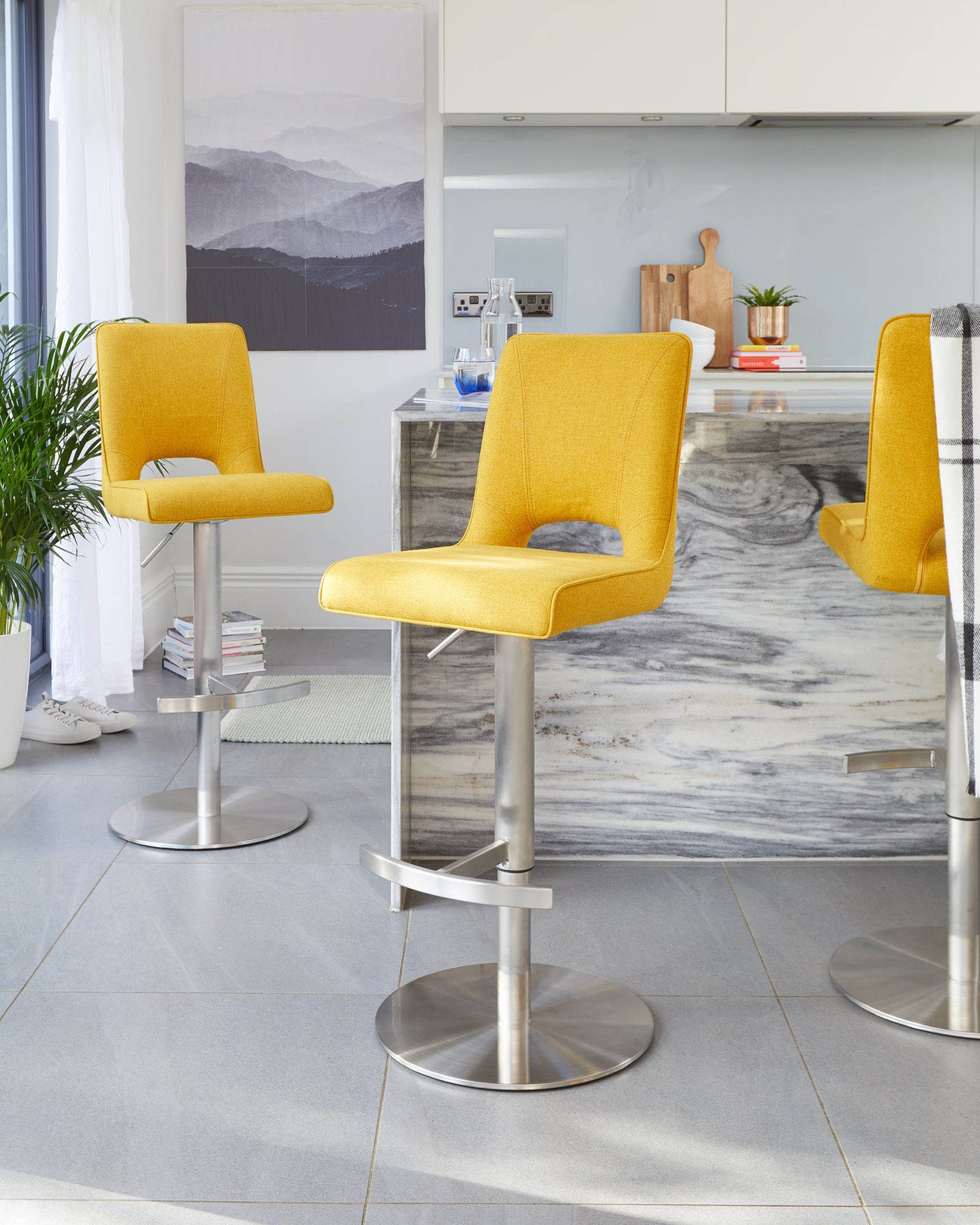 Two contemporary yellow bar stools with backs, featuring sleek armrests and padded seats, mounted on adjustable, swivel brushed metal bases.