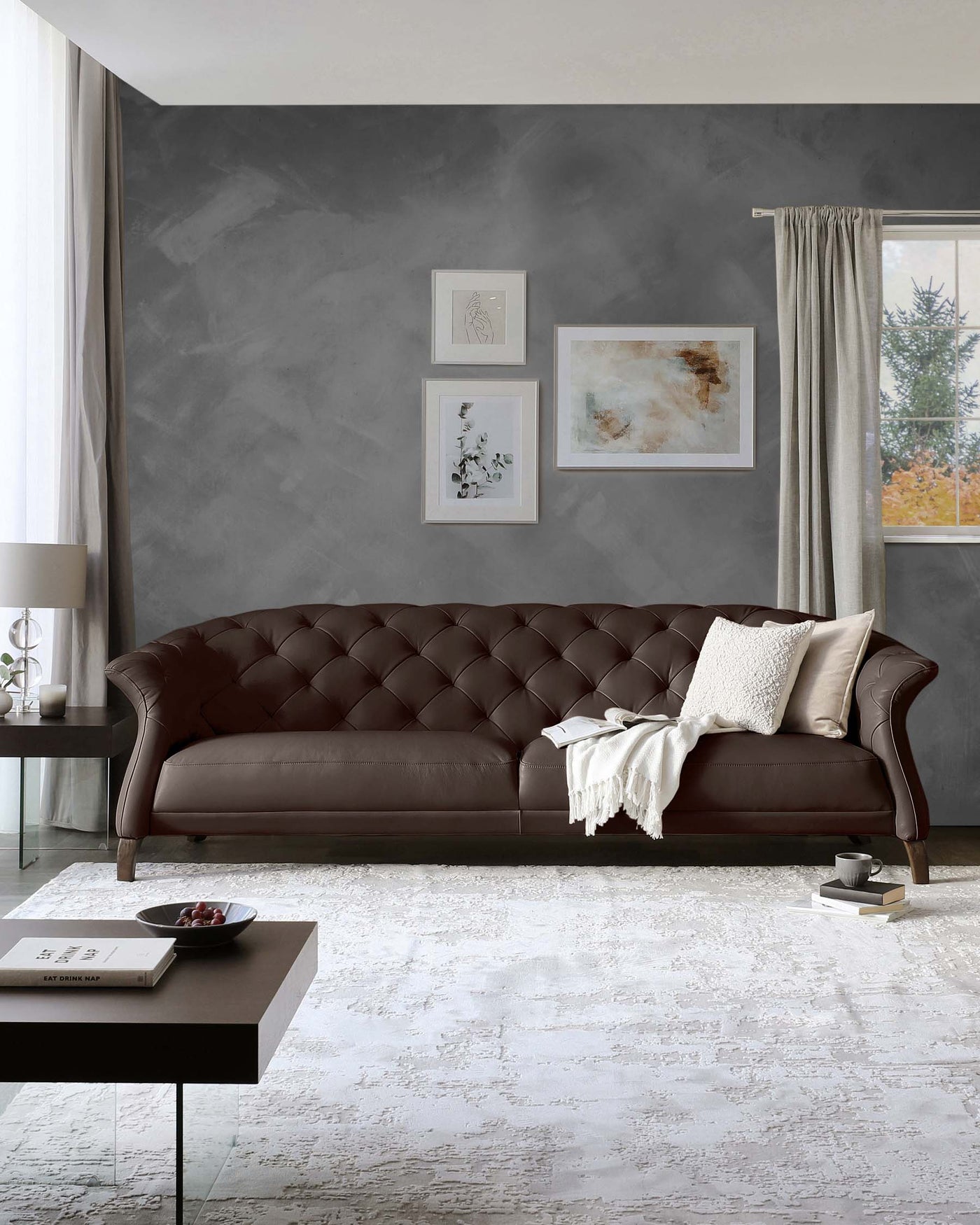 Elegant living room featuring a classic chesterfield sofa in dark brown leather with tufted back and arms, decorative cushions, and a cosy off-white throw. A sleek, modern side table with a dark finish and a simple, understated coffee table complement the sofa.
