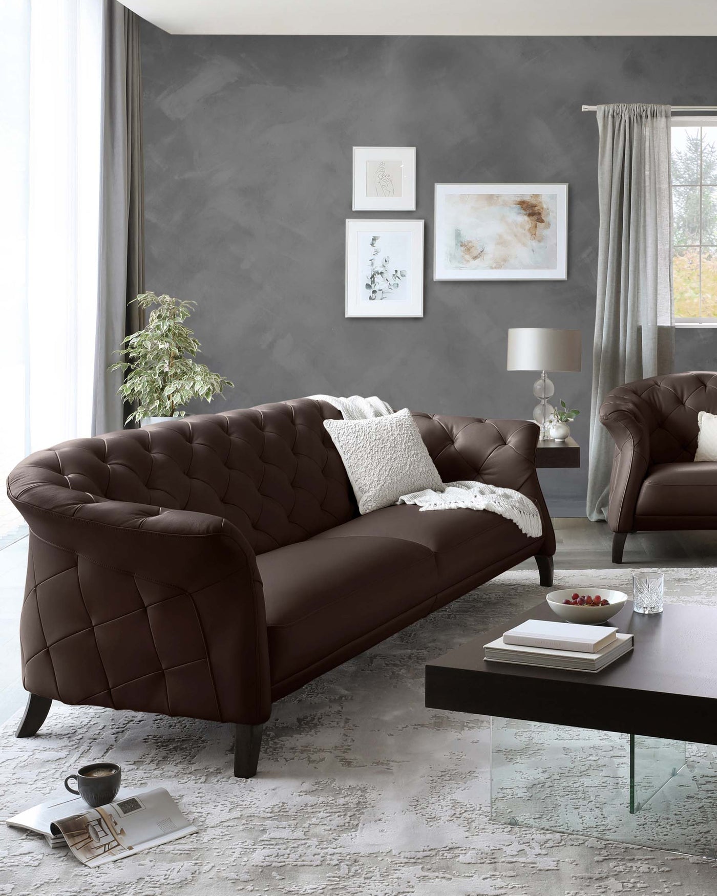 Elegant brown tufted leather sofa with matching armchair, complemented by a glass-top coffee table with dark wooden base, set against a distressed white rug.