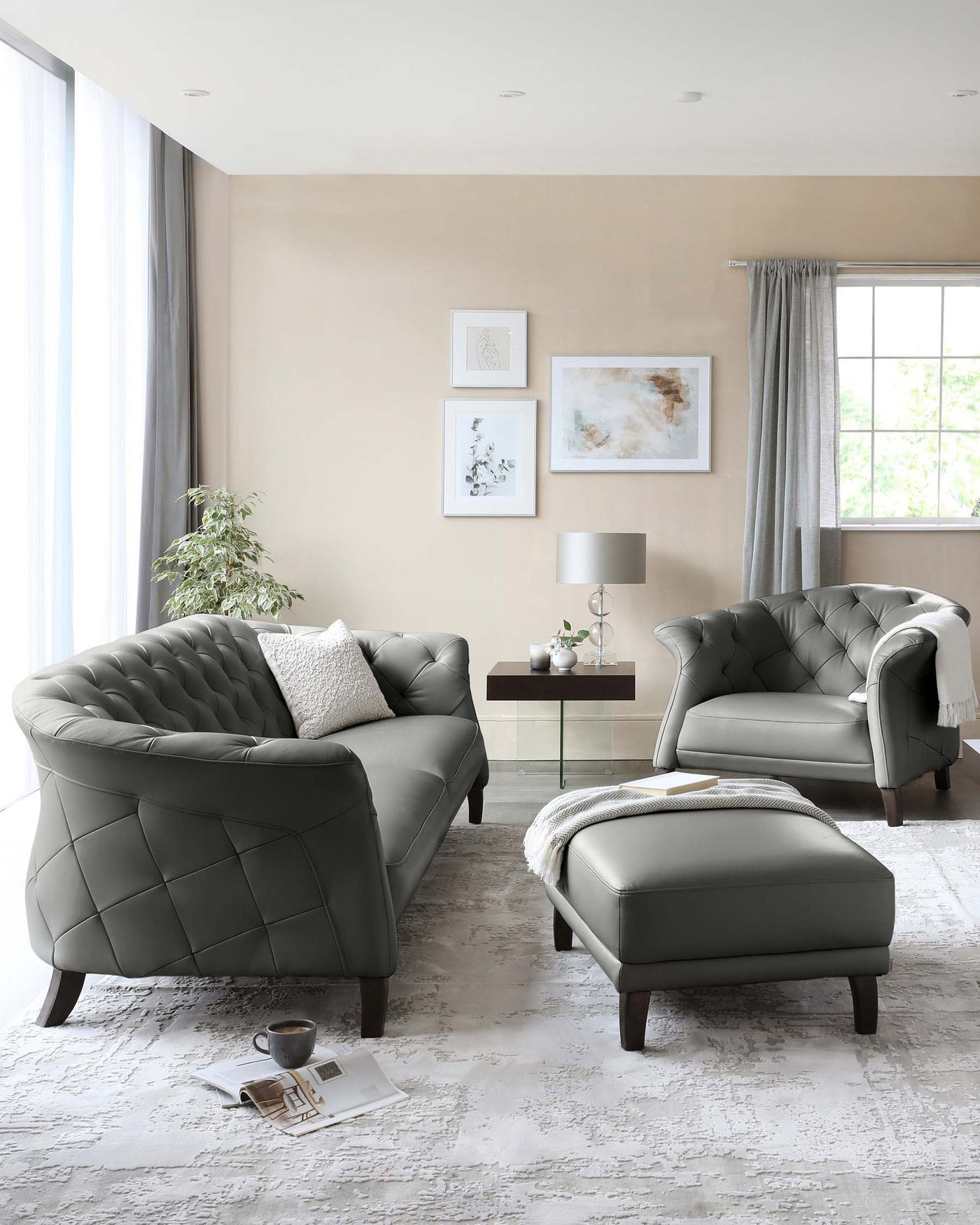 Elegant living room furniture set featuring a tufted charcoal grey sofa with matching armchair and ottoman, all with dark wooden legs. A contemporary side table with a lamp and decorative items, along with a light grey textured area rug, complete the ensemble.