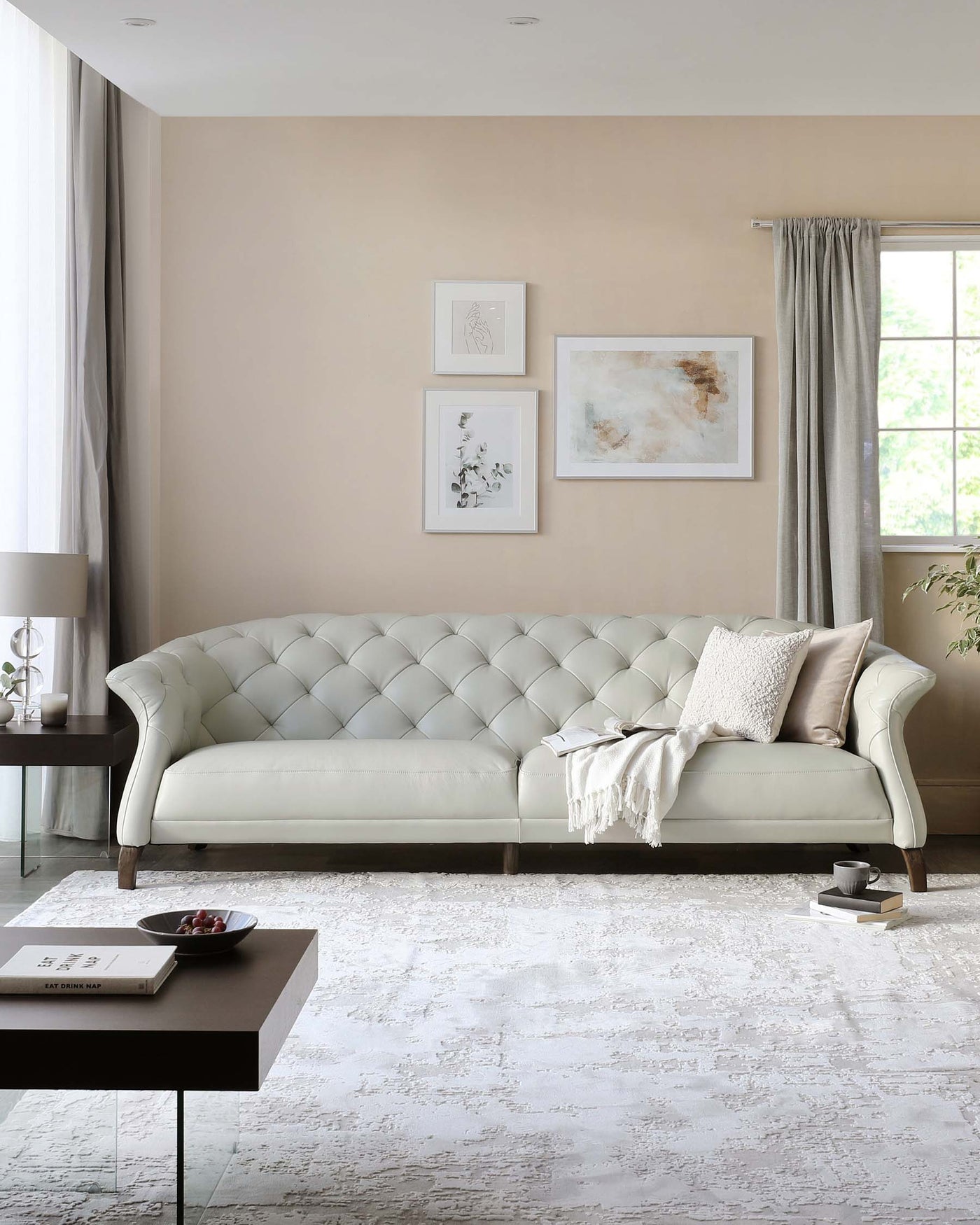 Elegant tufted back pale green sofa with graceful curved arms, complemented by a dark wood side table and a minimalist dark coffee table with a book and cup.