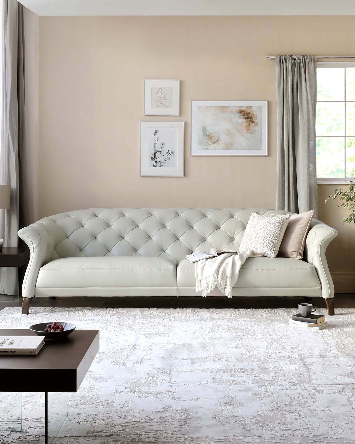 Elegant traditional tufted back cream sofa with curved armrests and dark wooden legs, accompanied by a modern square coffee table with a black top and thin metal legs, set on a distressed white patterned area rug.