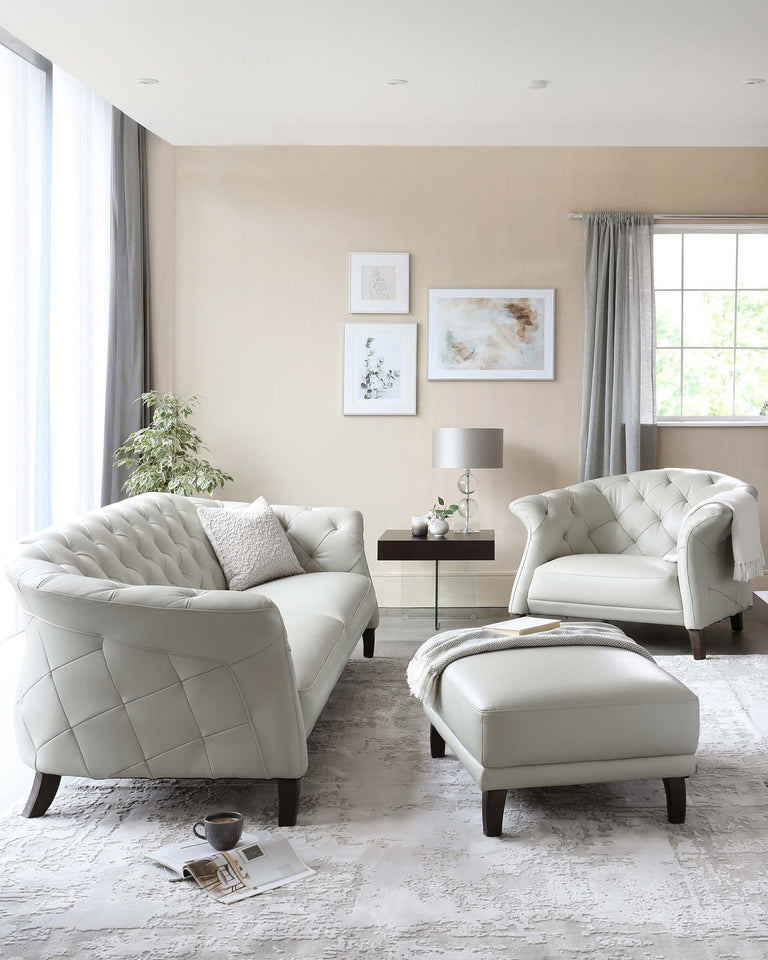 Elegant living room furniture set featuring a light tan, tufted leather sofa with matching armchair, complemented by a rectangular ottoman. The set is accessorized with throw pillows and a blanket, positioned on a textured area rug. A side table with a lamp and decorative vase completes the arrangement.