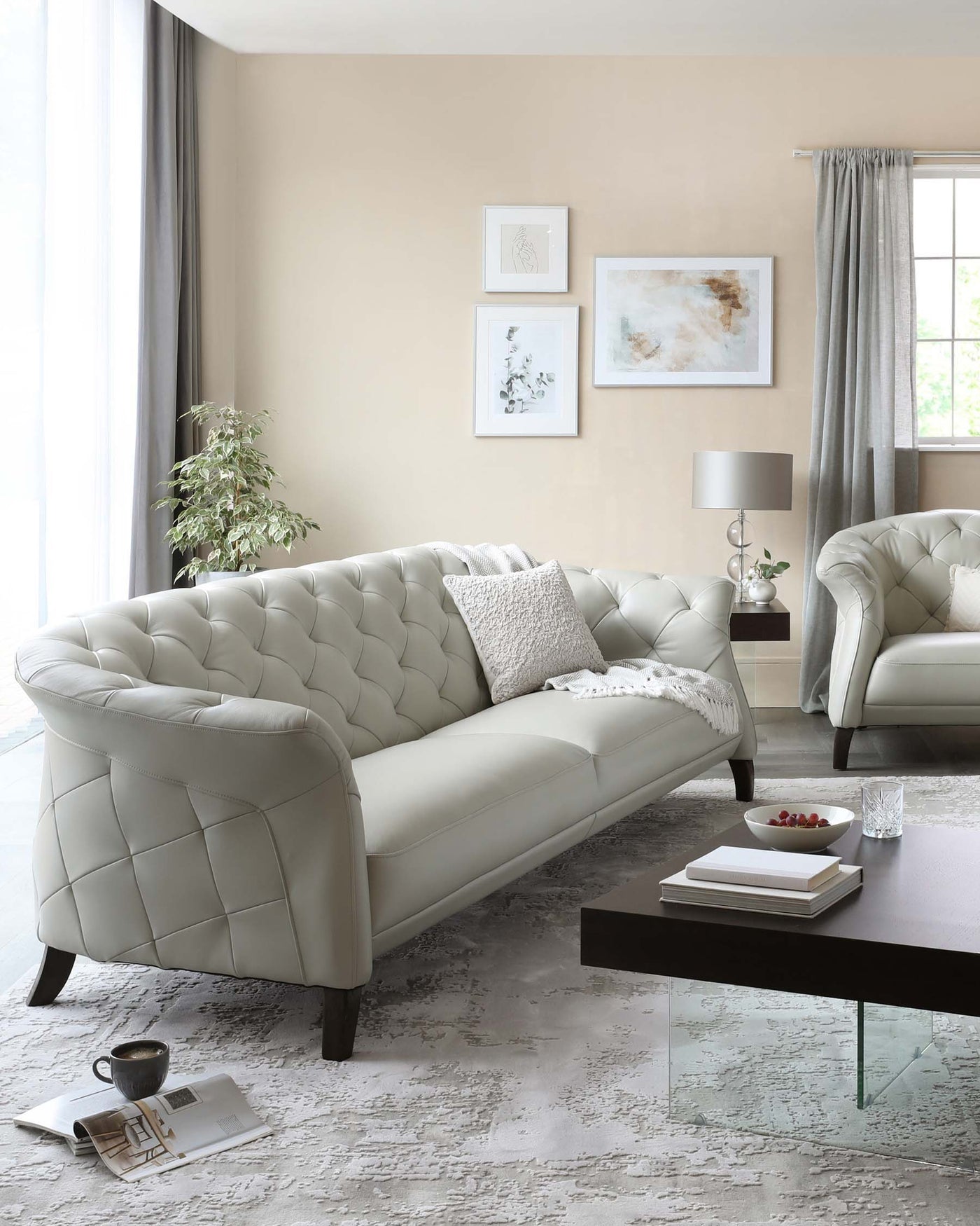 Elegant modern living room set featuring a tufted ivory sofa with curved armrests, matching armchair, dark rectangular wooden coffee table with a glass insert, and coordinating side table with a lamp, all arranged on a distressed cream and grey area rug.