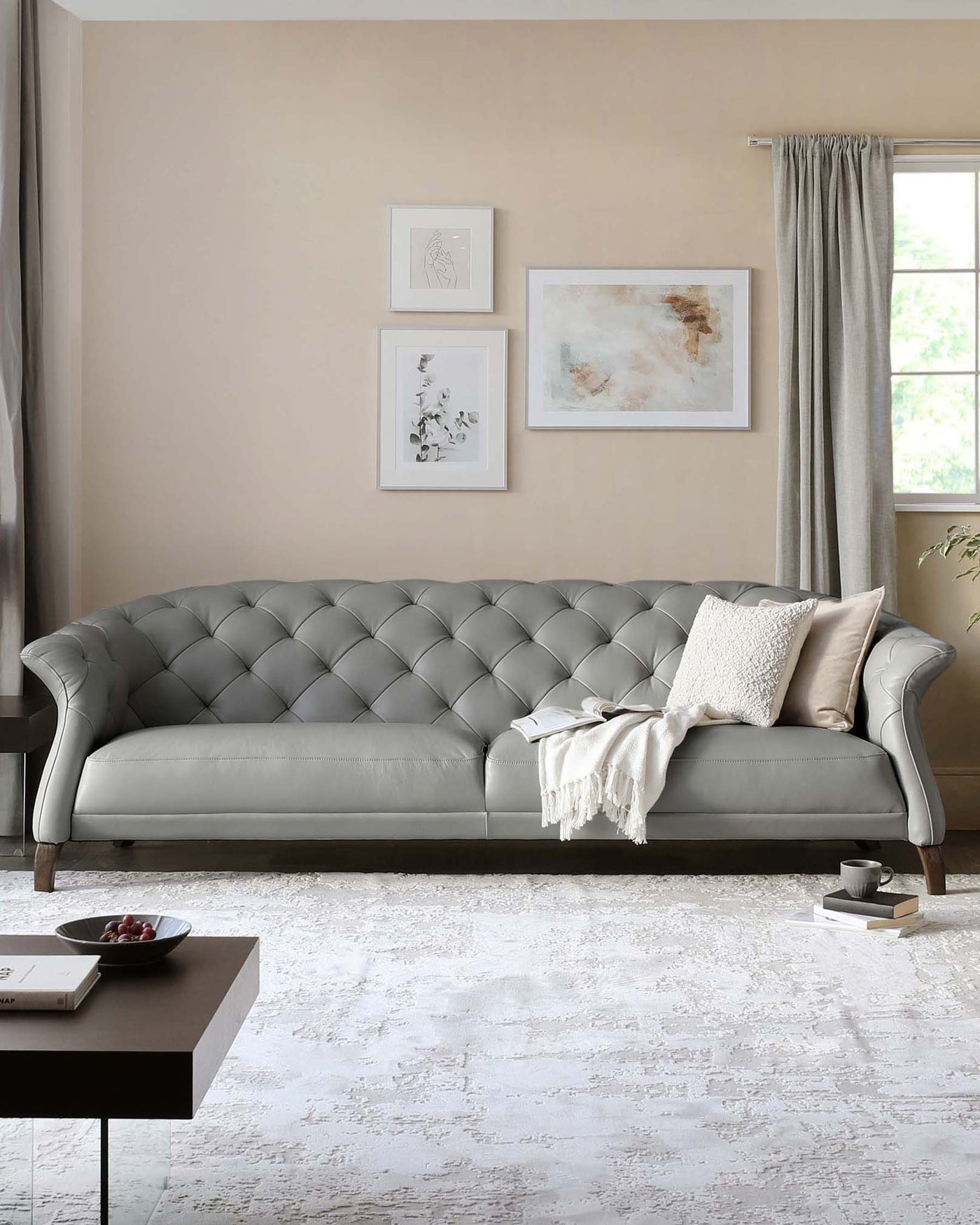 Elegant tufted back grey sofa with scrolled armrests on wooden legs, paired with a modern black square coffee table on an abstract-patterned off-white area rug.